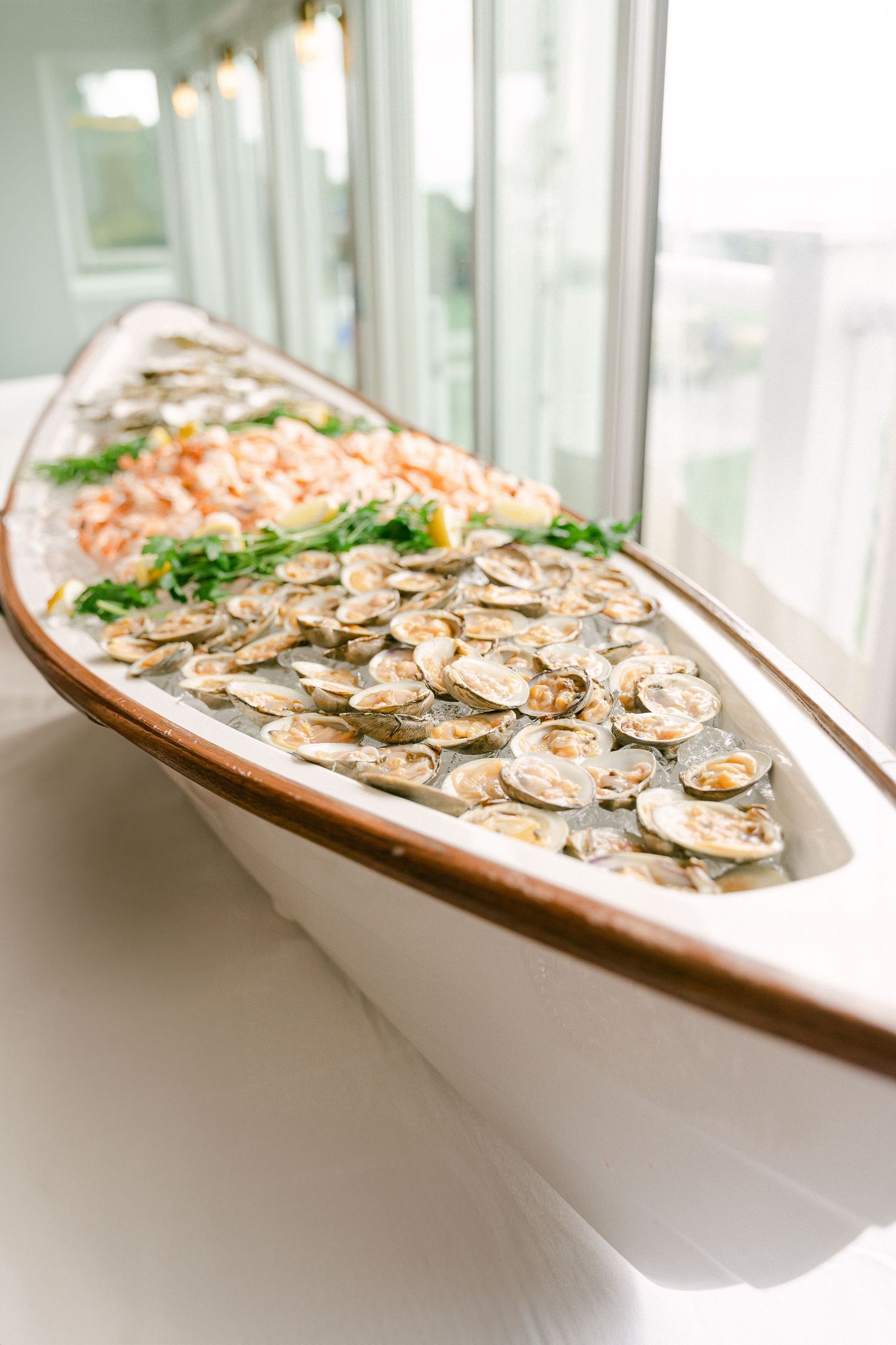 Elegant seafood display in a wooden boat vessel filled with fresh oysters, shrimp, and garnishes on ice in Cape Cod