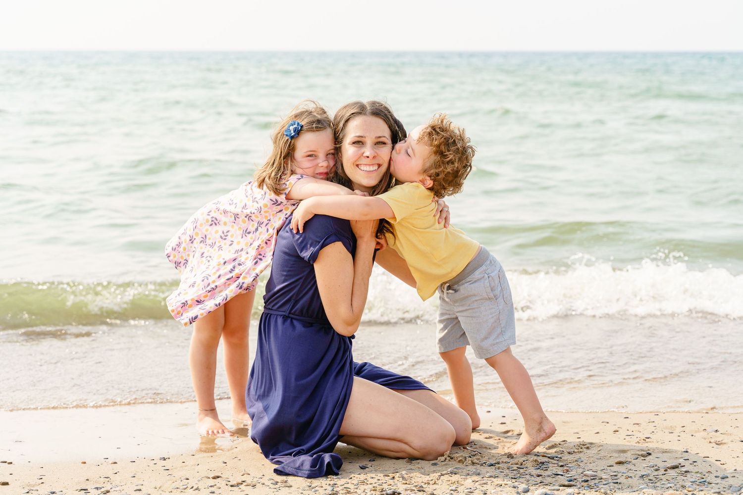 Family enjoying a playful moment together on a sunny beach with waves in the background.