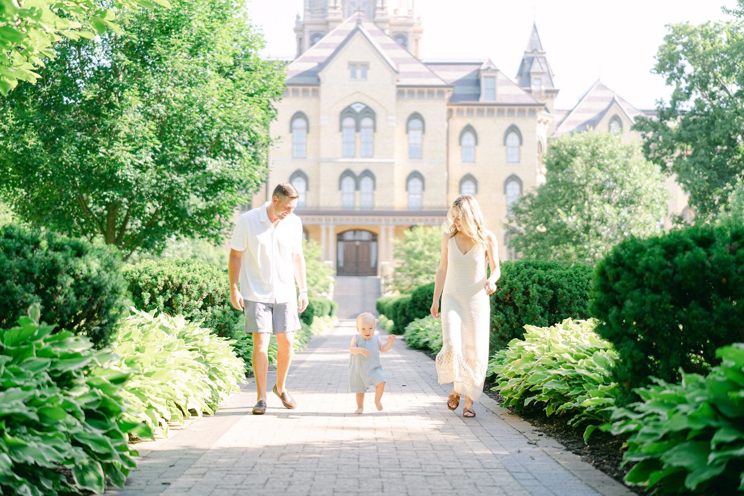 Family walking along a garden path towards a historic church with Gothic architecture on a sunny day.