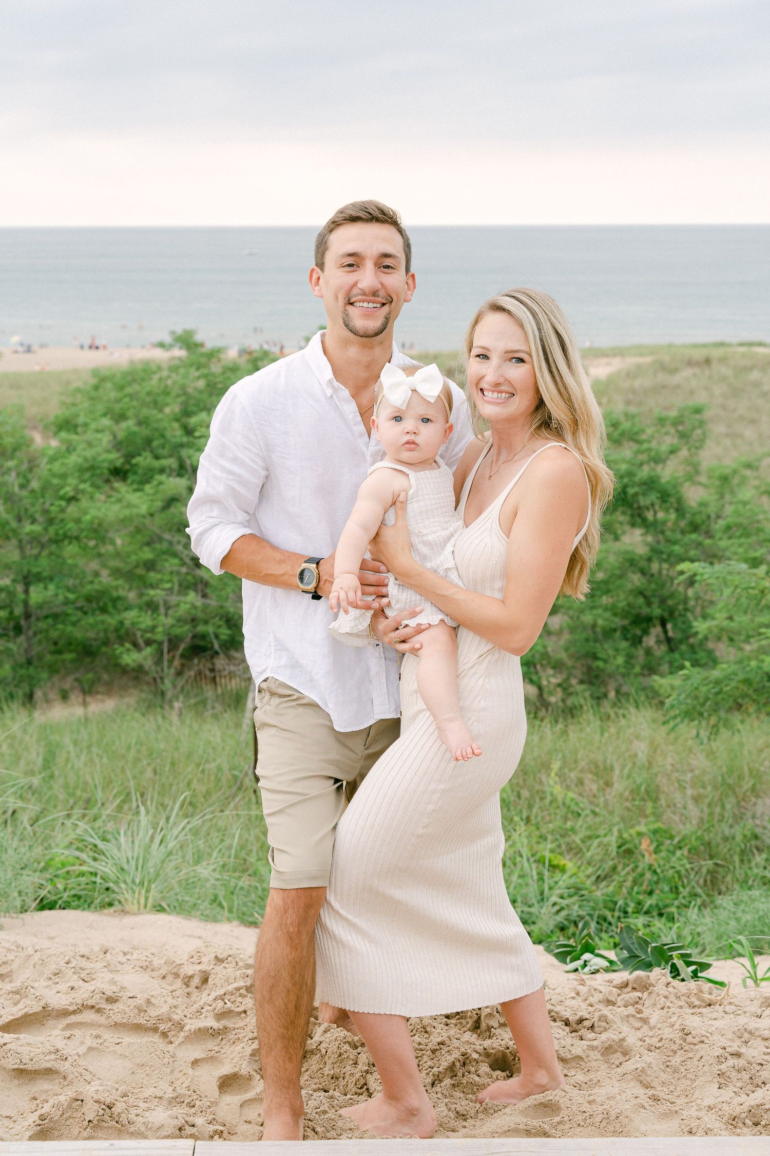 Happy family in coordinating white and beige outfits share joyful moments on a coastal hillside.
