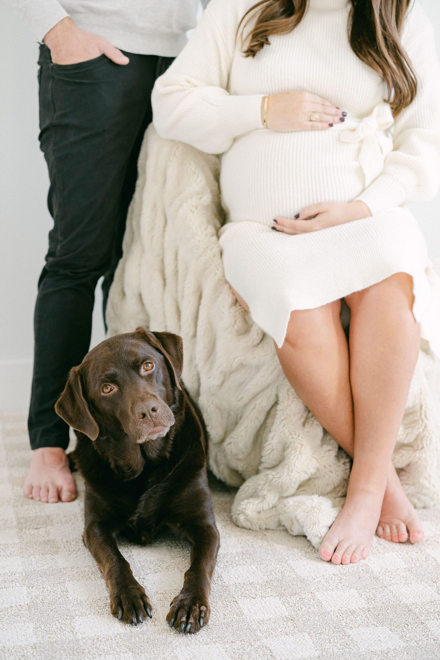 A chocolate Labrador dog lies beside someone wearing a white sweater on a light-colored floor in a series of photos.