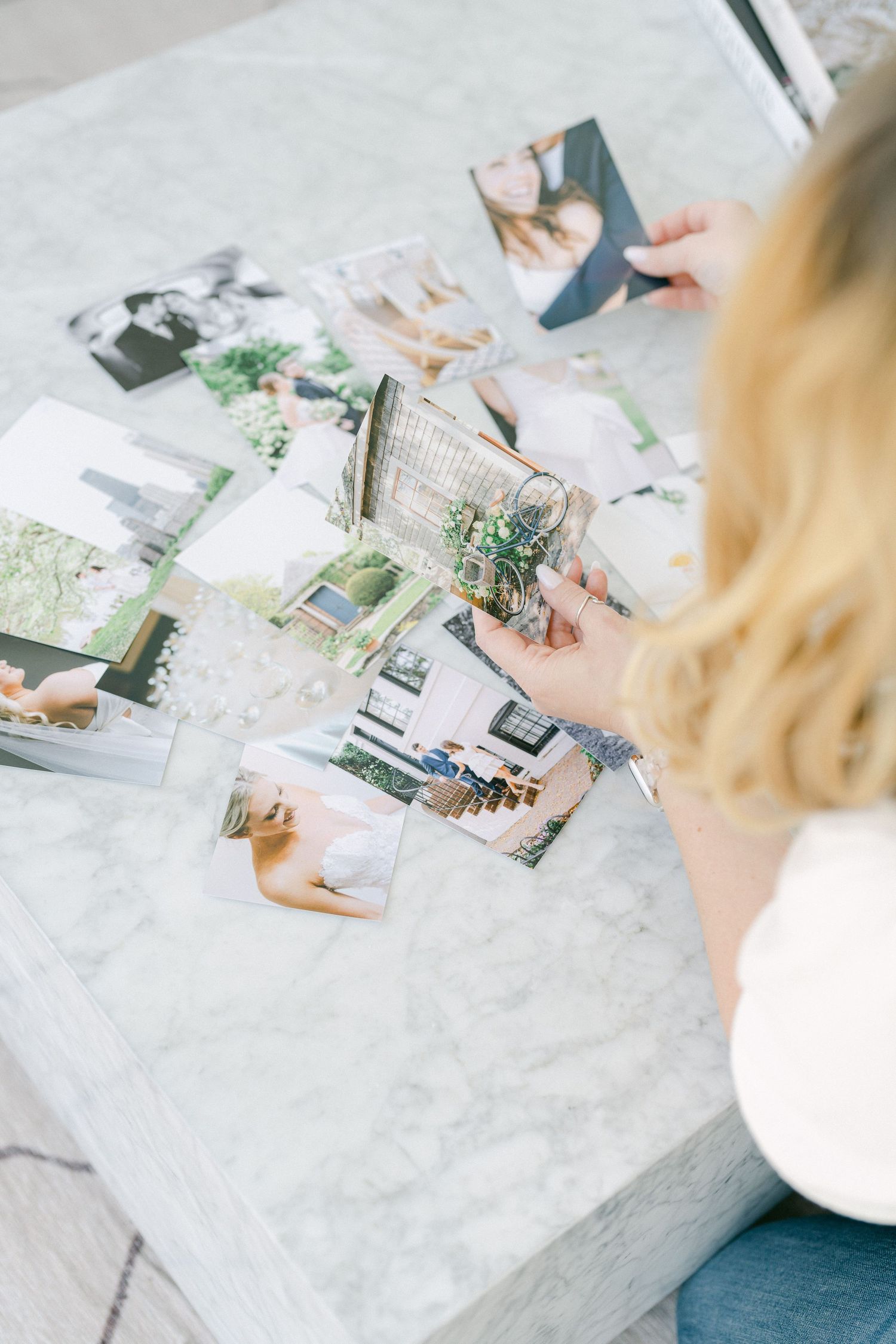 Hands working on creative photo layout and design elements on a white marble surface.