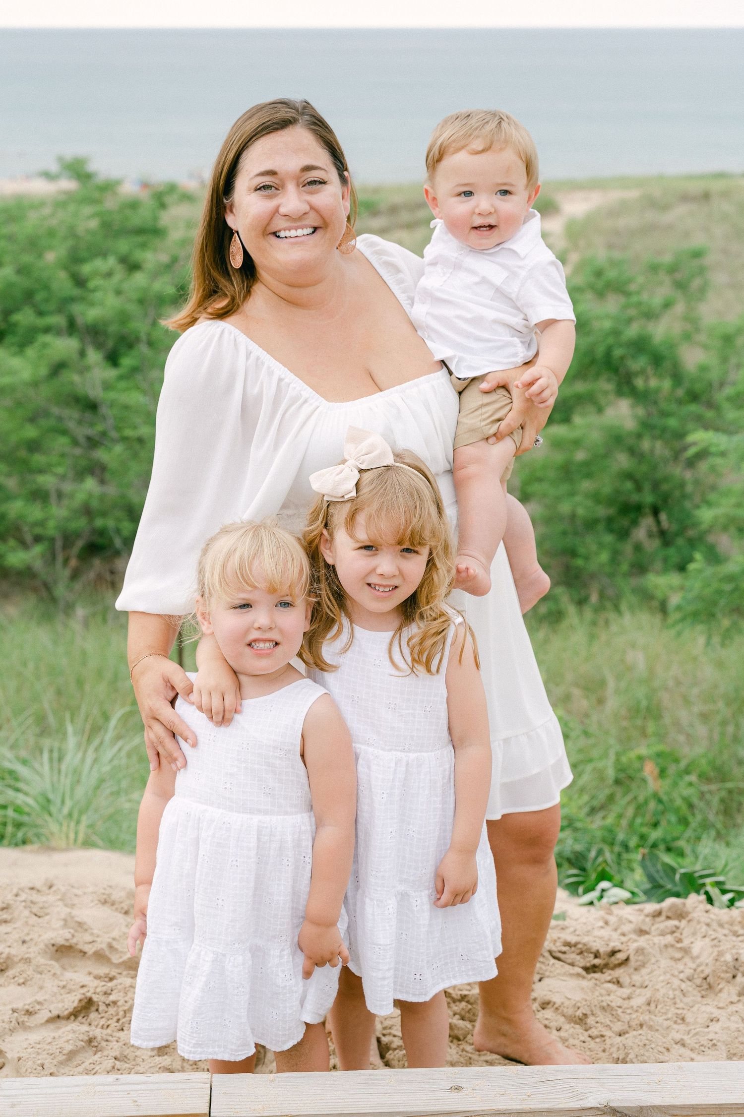 Group portrait in white outfits on sandy beach hill with ocean view.