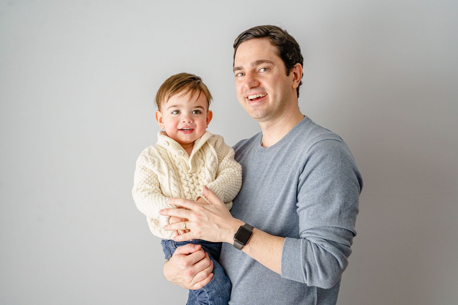 Joyful portrait of parent and child against light gray background.