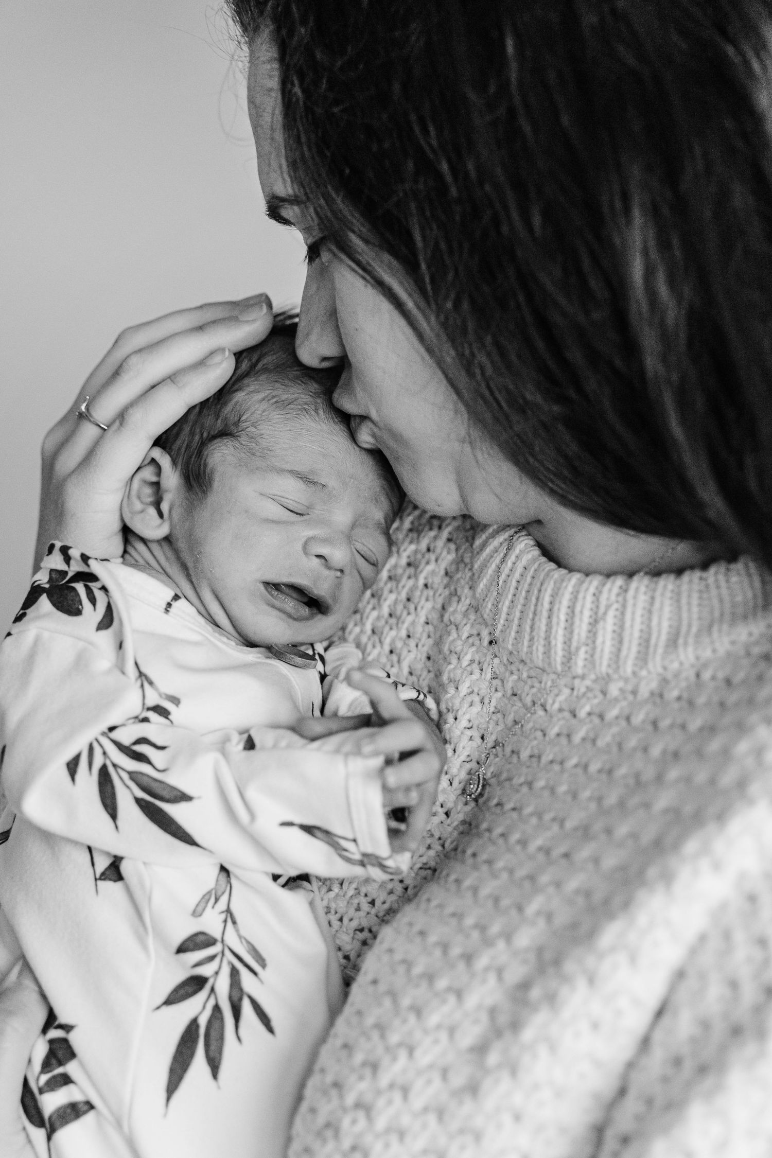 A tender black and white moment showing a newborn baby in a floral outfit being held close in a knit sweater.