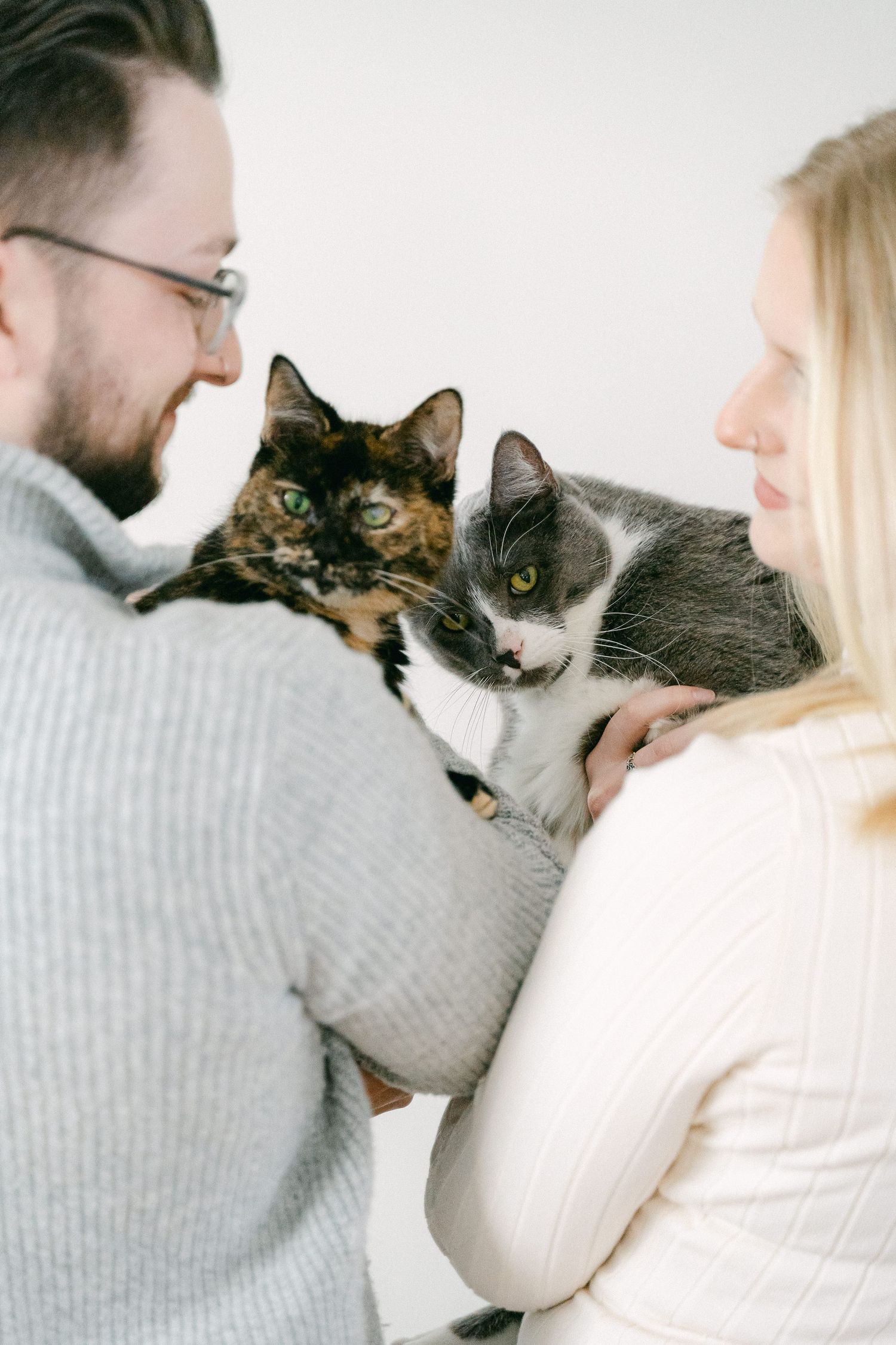 A couple in white and gray sweaters cuddle with their calico cat in a series of sweet candid moments.