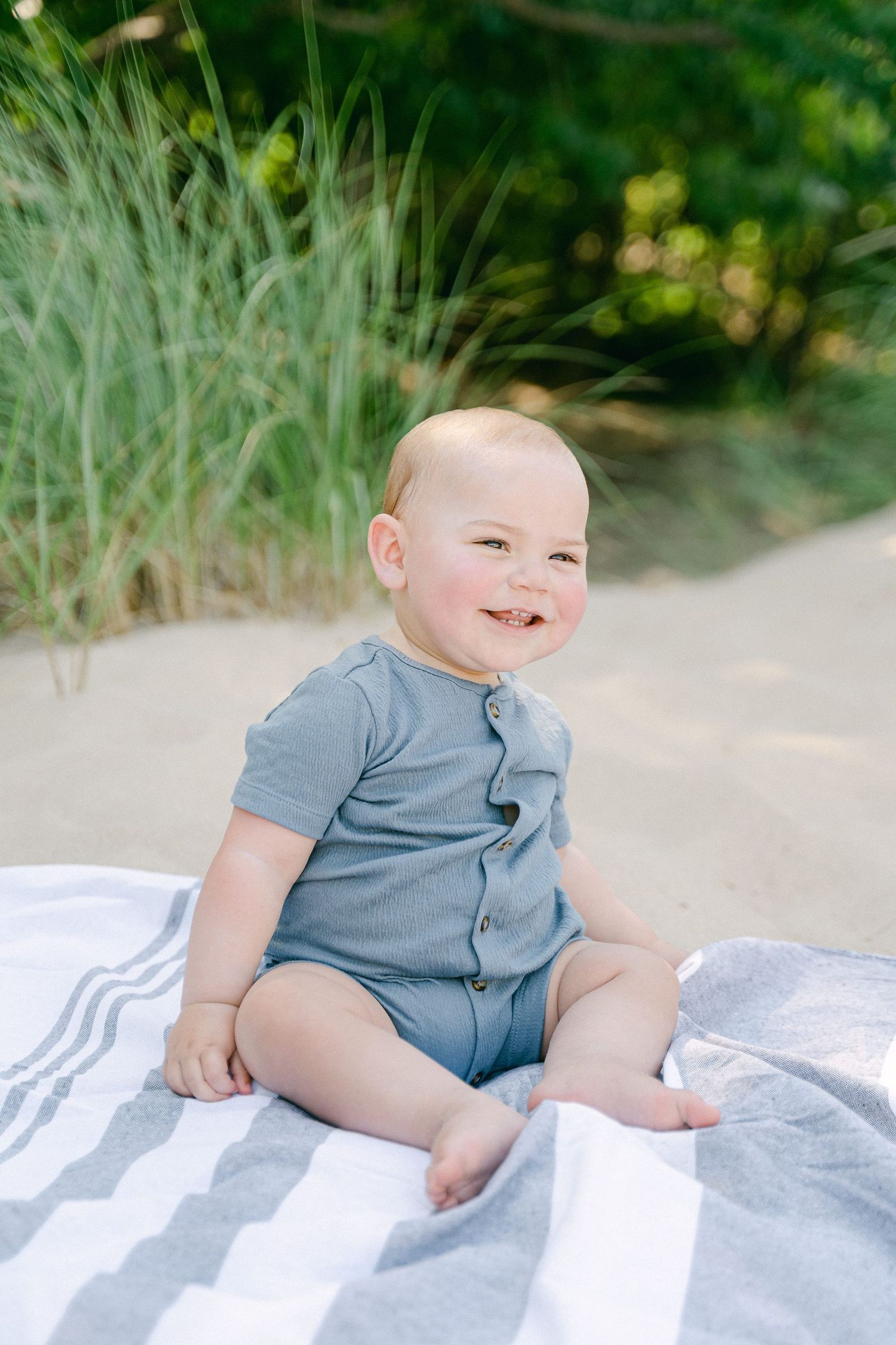 A sequence of four photos showing a baby in a gray outfit sitting and smiling on a white blanket outdoors.