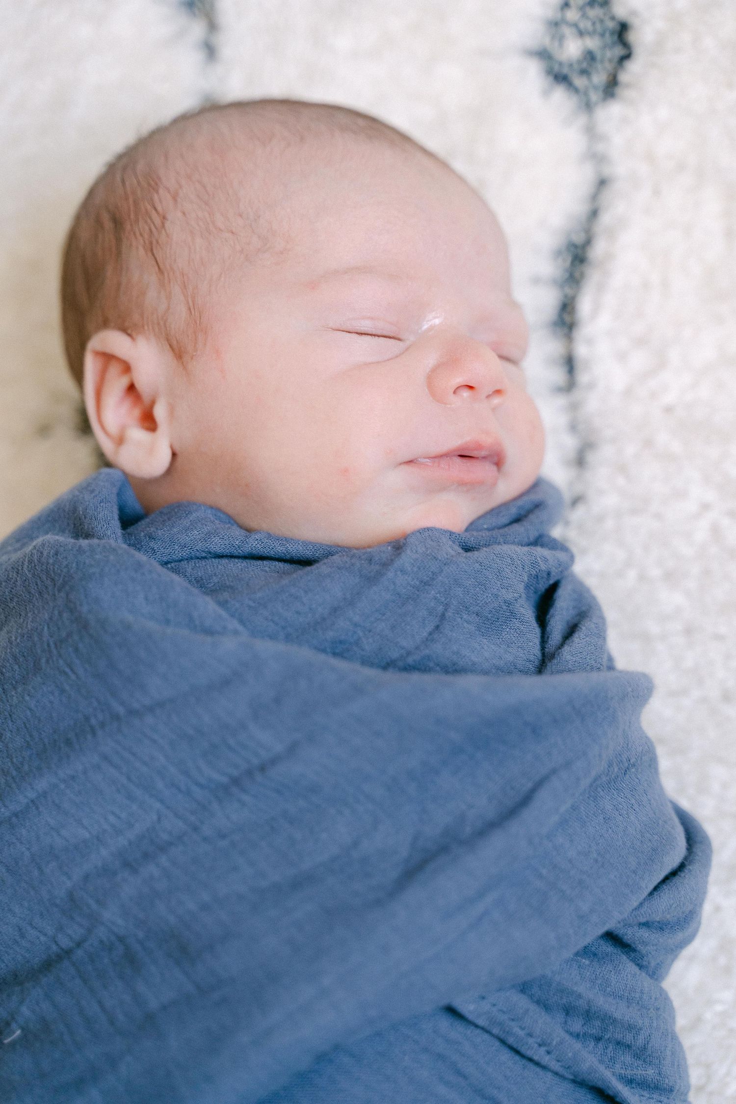 A sleeping newborn baby wrapped in a soft blue blanket against a white textured background.