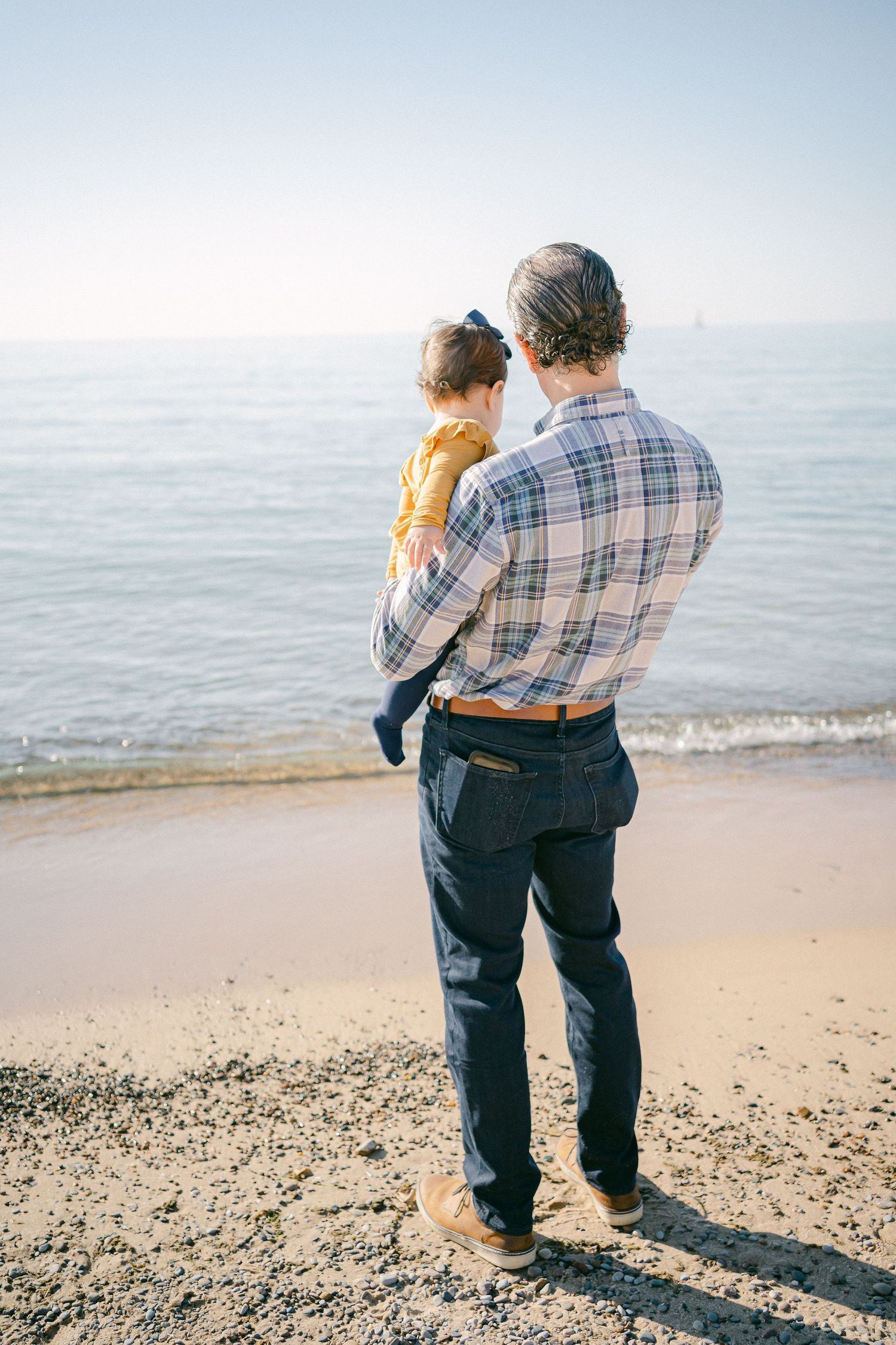 Couple in casual attire walking along a peaceful beach shoreline on a sunny afternoon.