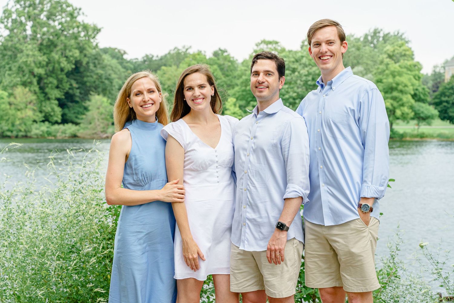 Four people pose for a casual summer portrait by a lake wearing coordinated blue and white clothing.