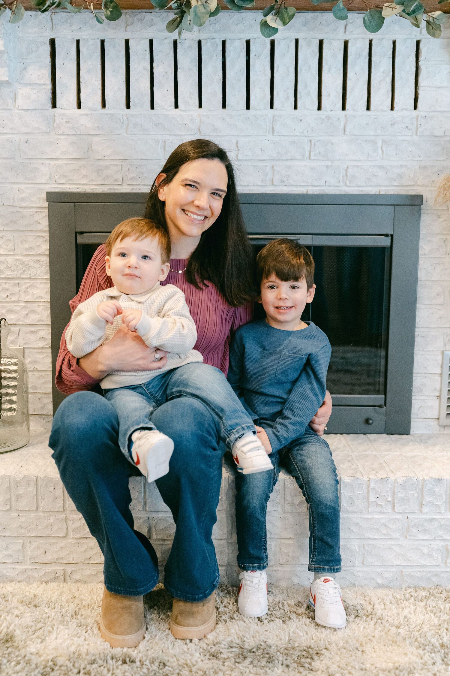 Family sitting together on a white brick fireplace hearth with greenery garland decoration above.