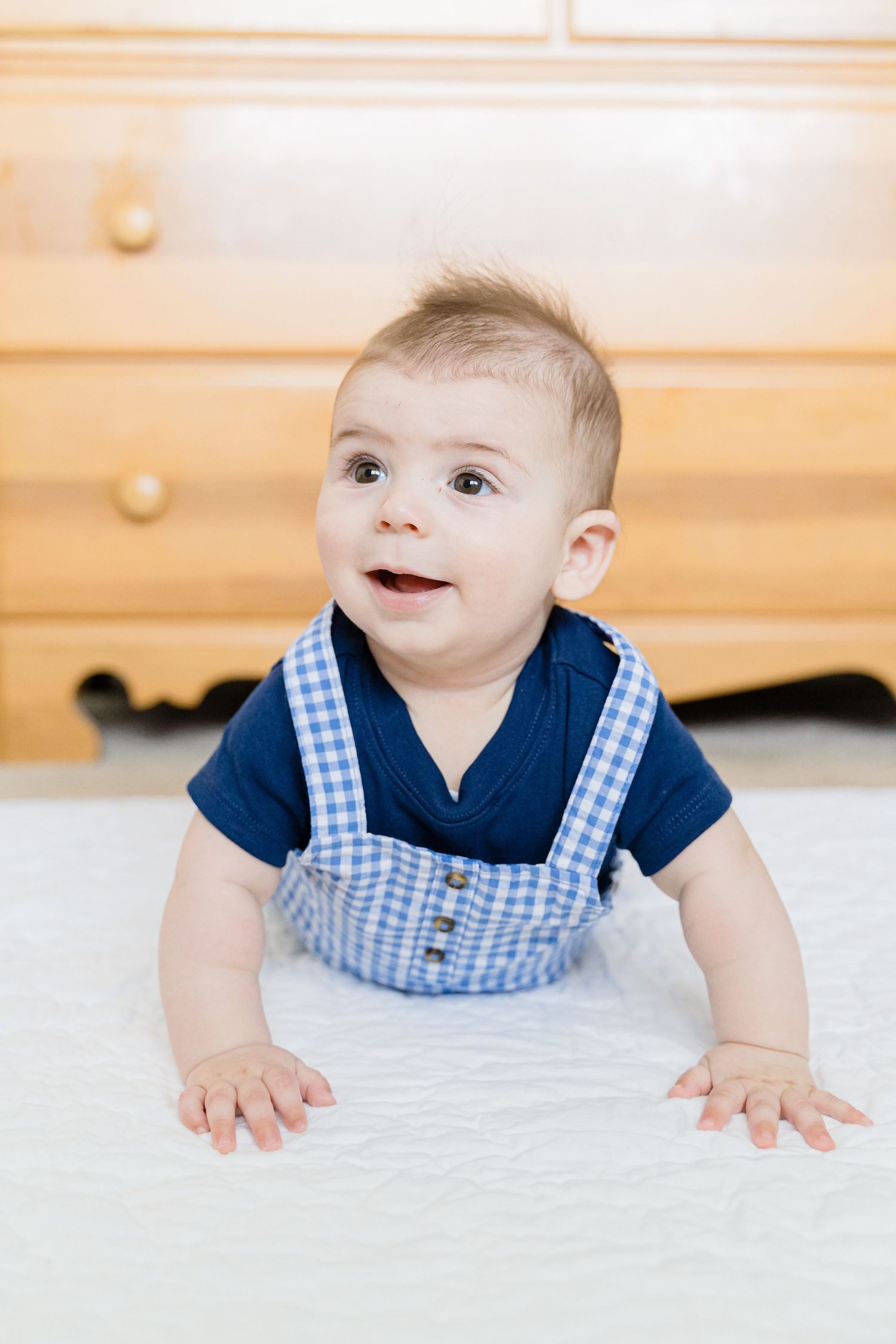Baby in navy and gingham outfit crawling on light colored carpet.
