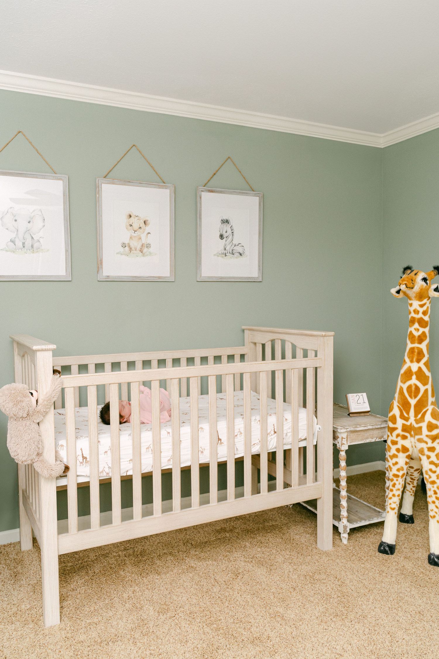 White cribs line a mint green nursery wall with plush animal decor and framed artwork above.