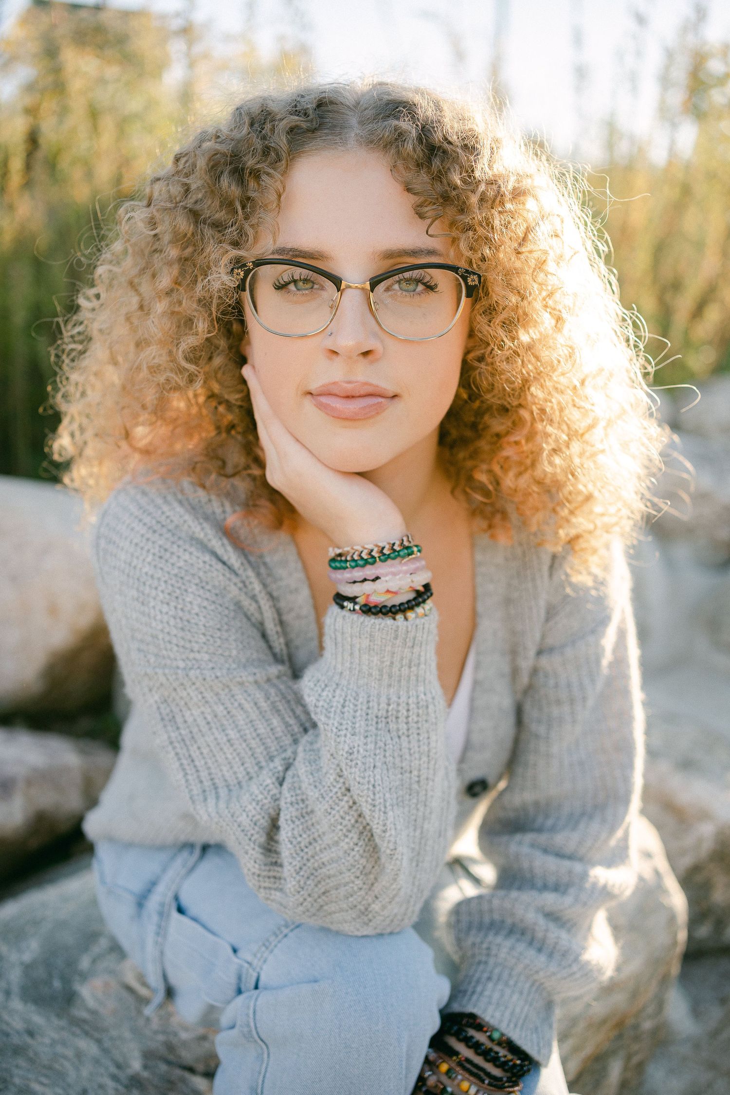 A series of outdoor portraits featuring curly hair, glasses, and a cozy gray sweater in natural sunlight.