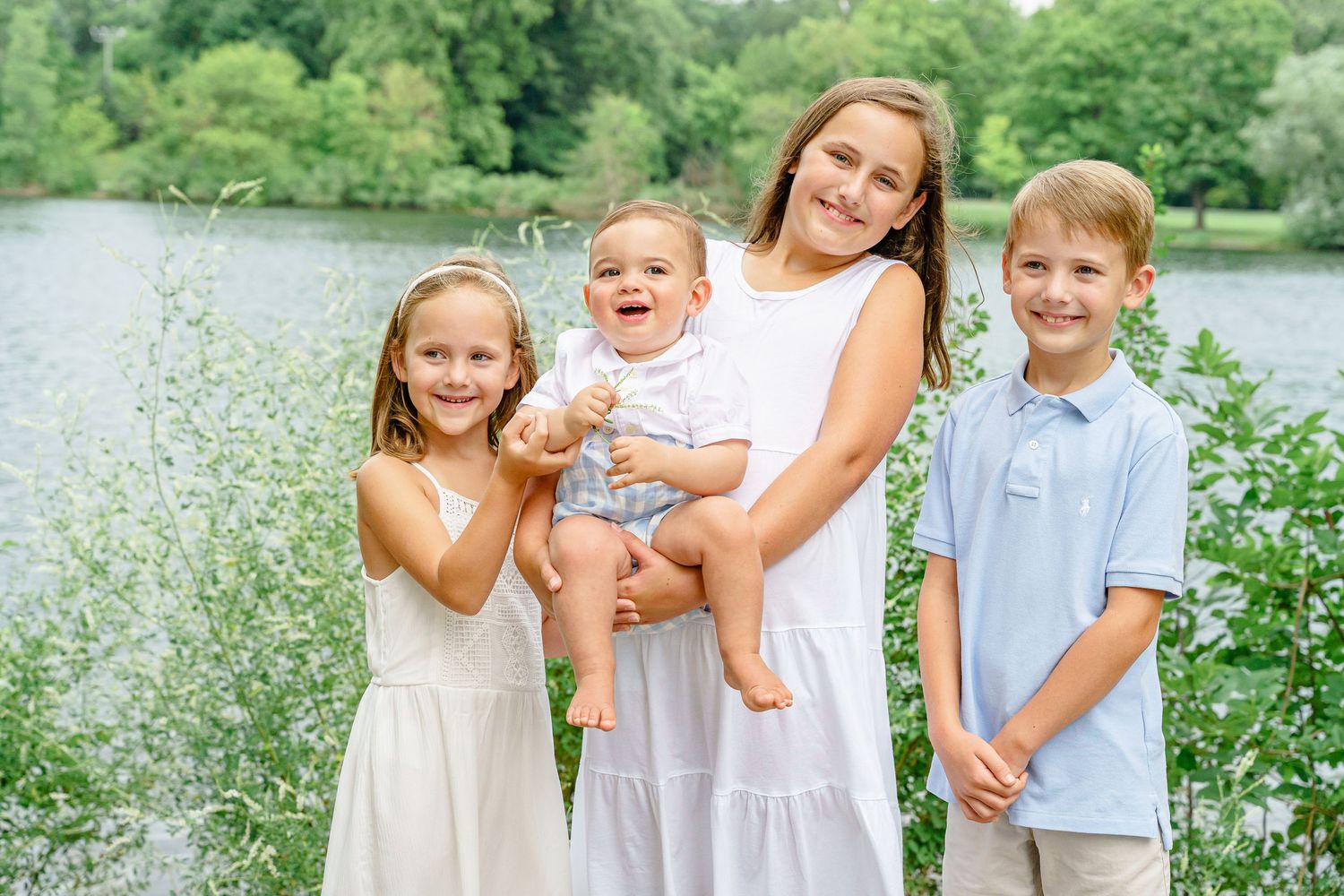 A group poses together outdoors near a lake with lush greenery in the background.