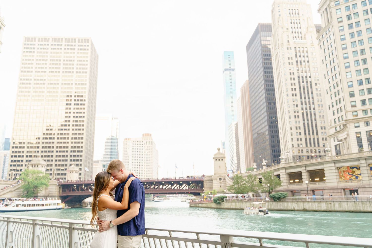 A couple shares a romantic moment along the Chicago Riverwalk with the city skyline in the background.