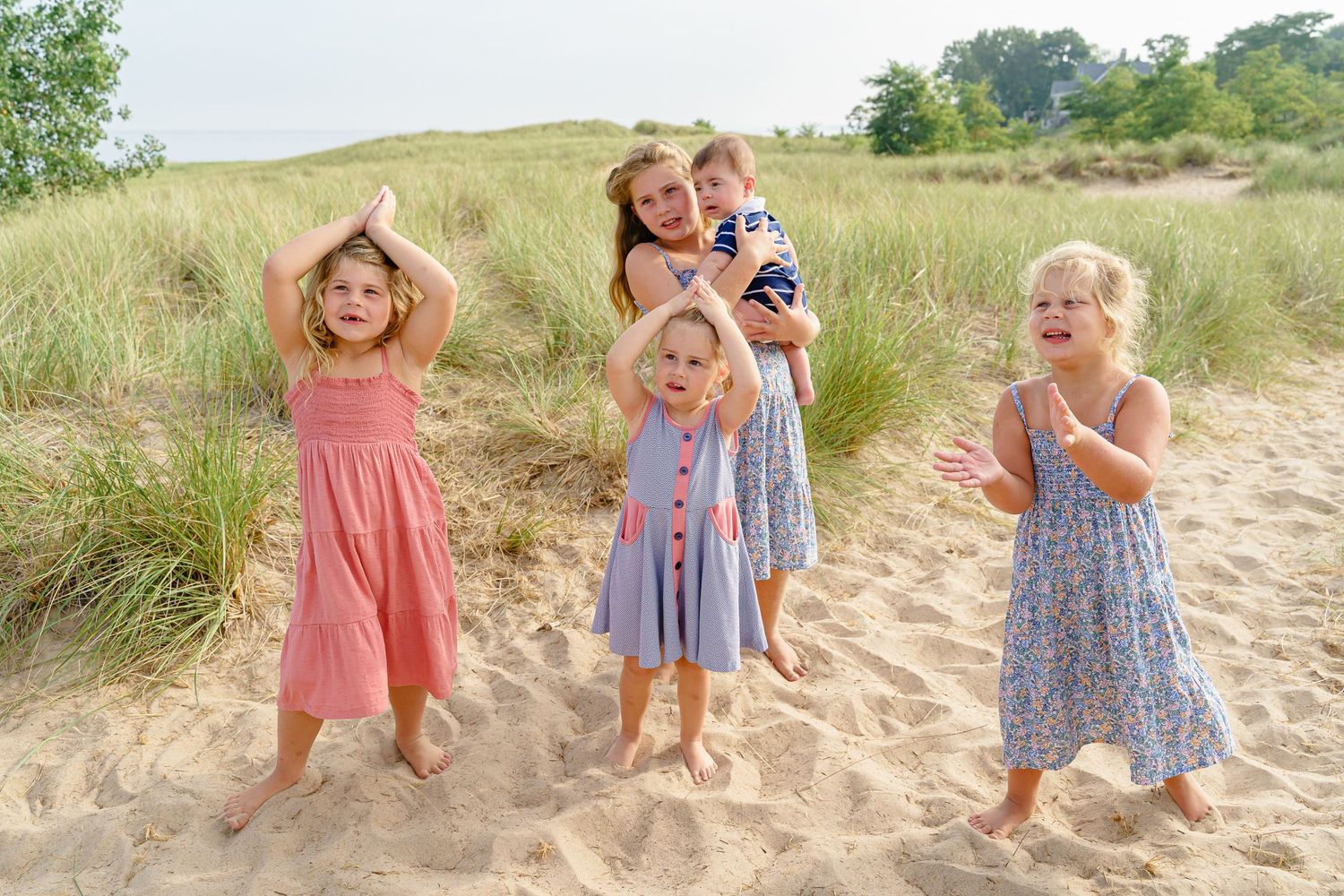 Children in matching dresses playing and running together on a sandy beach path during a summer day.
