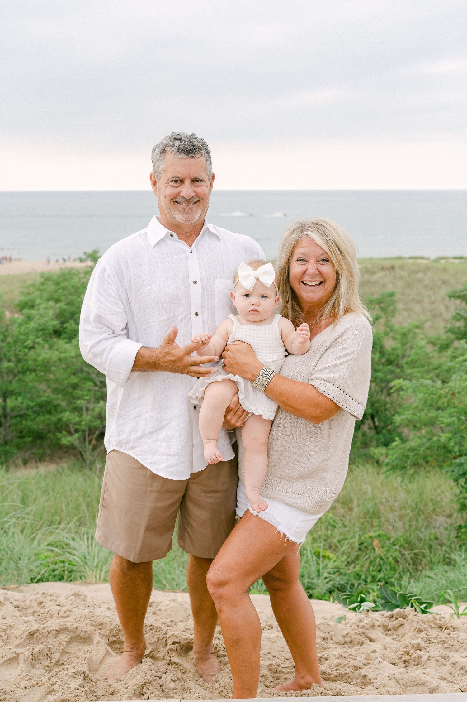Family portrait on sandy beach hill with ocean view and green vegetation in background.