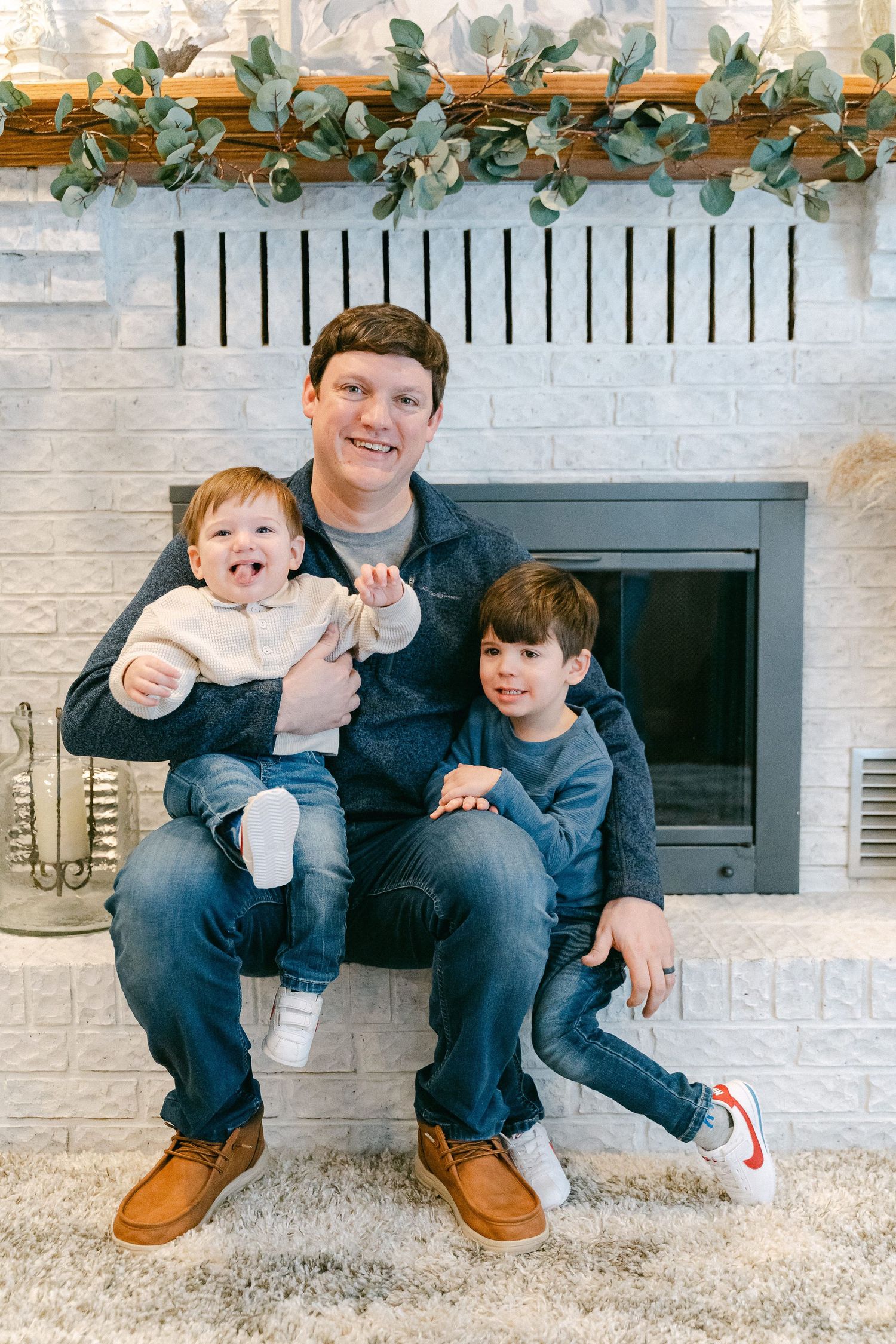 A family portrait in front of a white brick fireplace decorated with eucalyptus garland.
