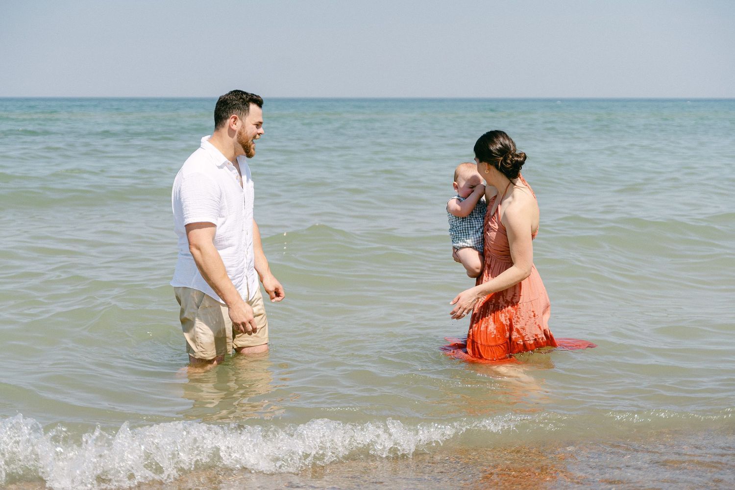 Family playing together in shallow ocean waves on a sunny summer day at the beach.