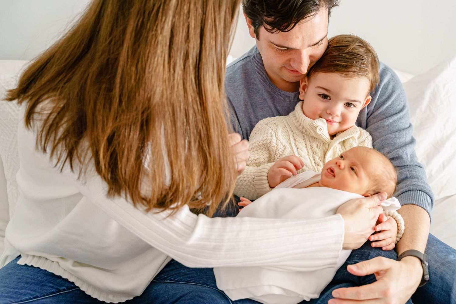 Parents and child share tender moments while cuddling together on white bedding during an intimate family photo session.