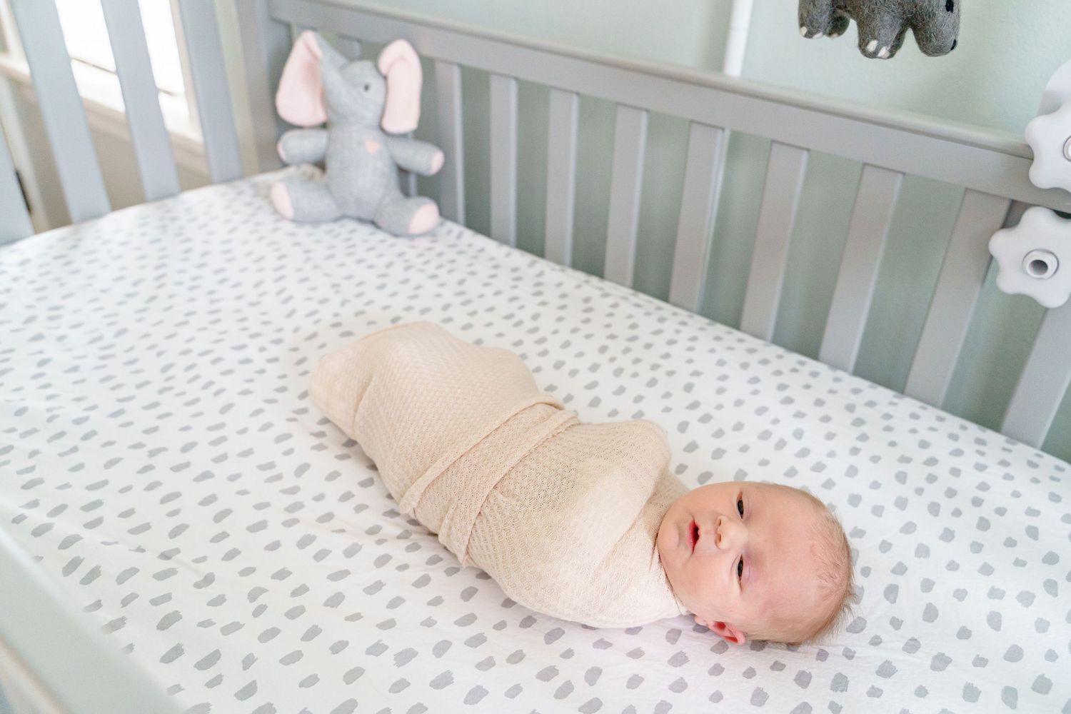A white crib with a polka dot mattress pad and soft beige bedding in a nursery setting.