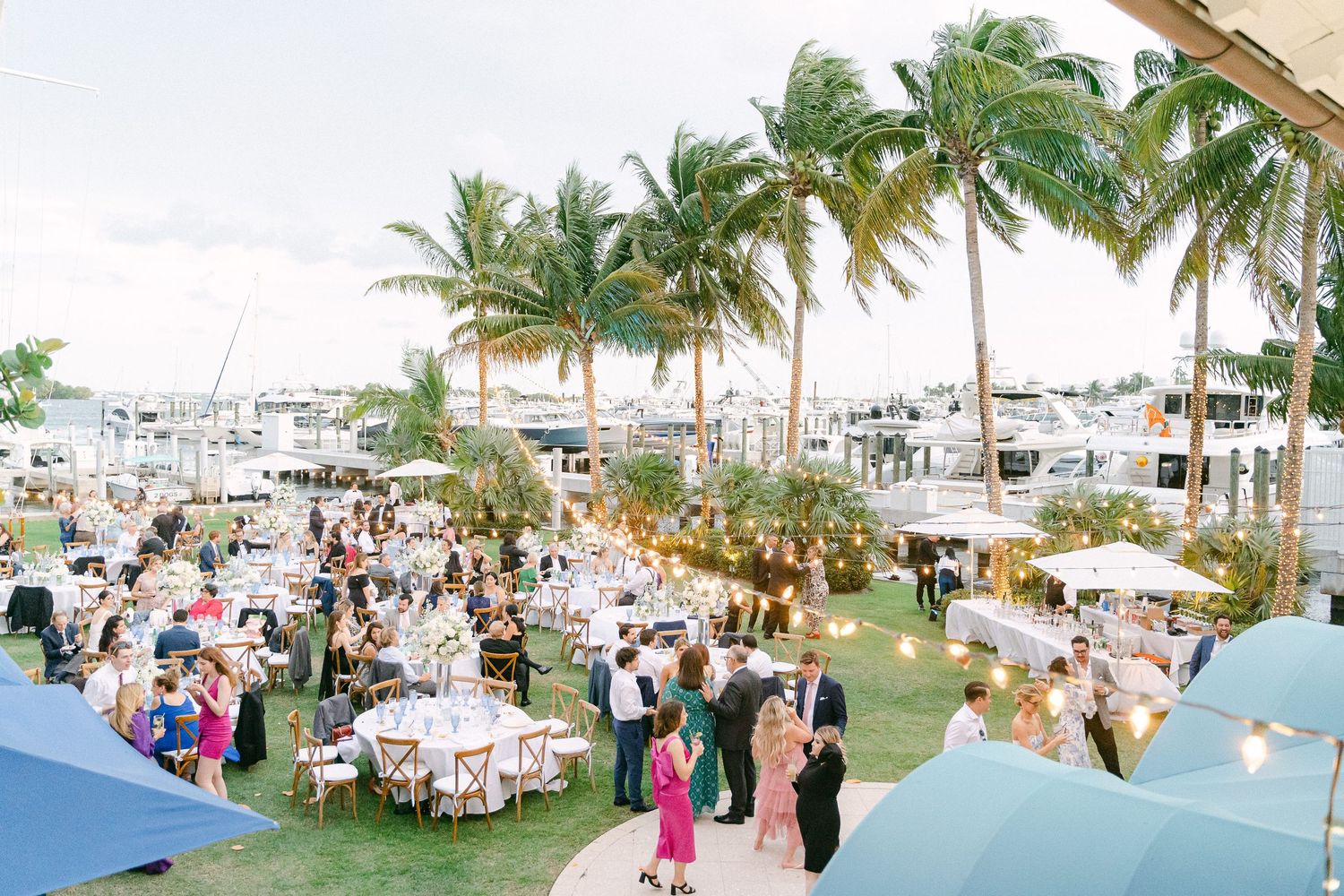 Elegant outdoor waterfront wedding reception with palm trees, string lights, and guests dining near a marina in Miami, FL
