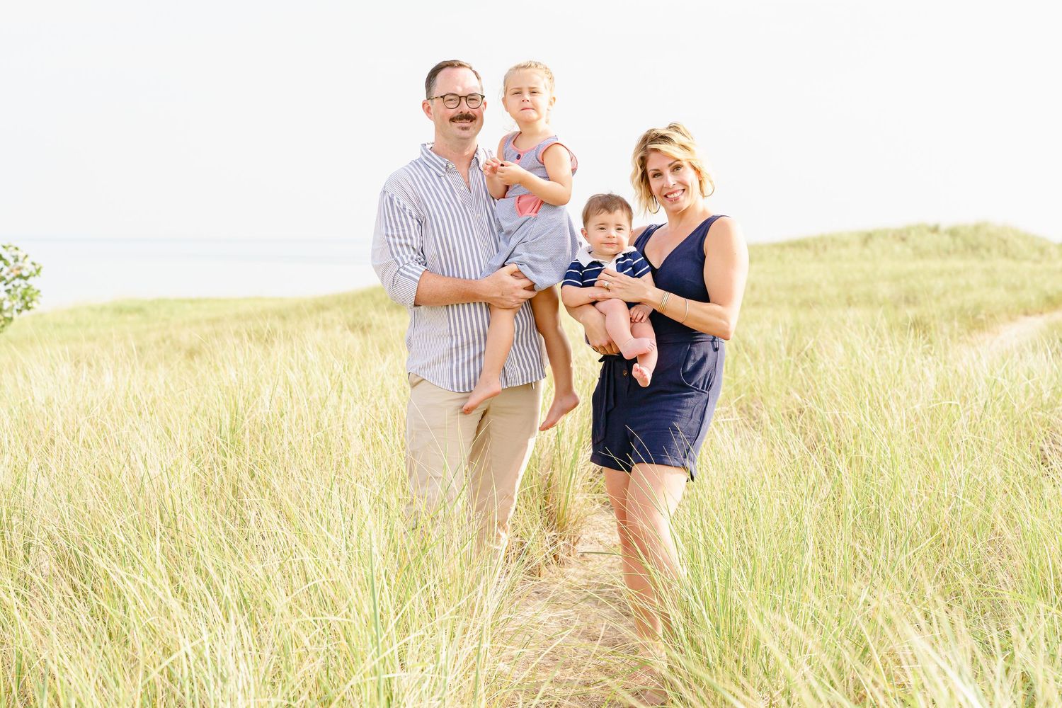 A family shares joyful moments together while posing in a golden meadow at sunset.