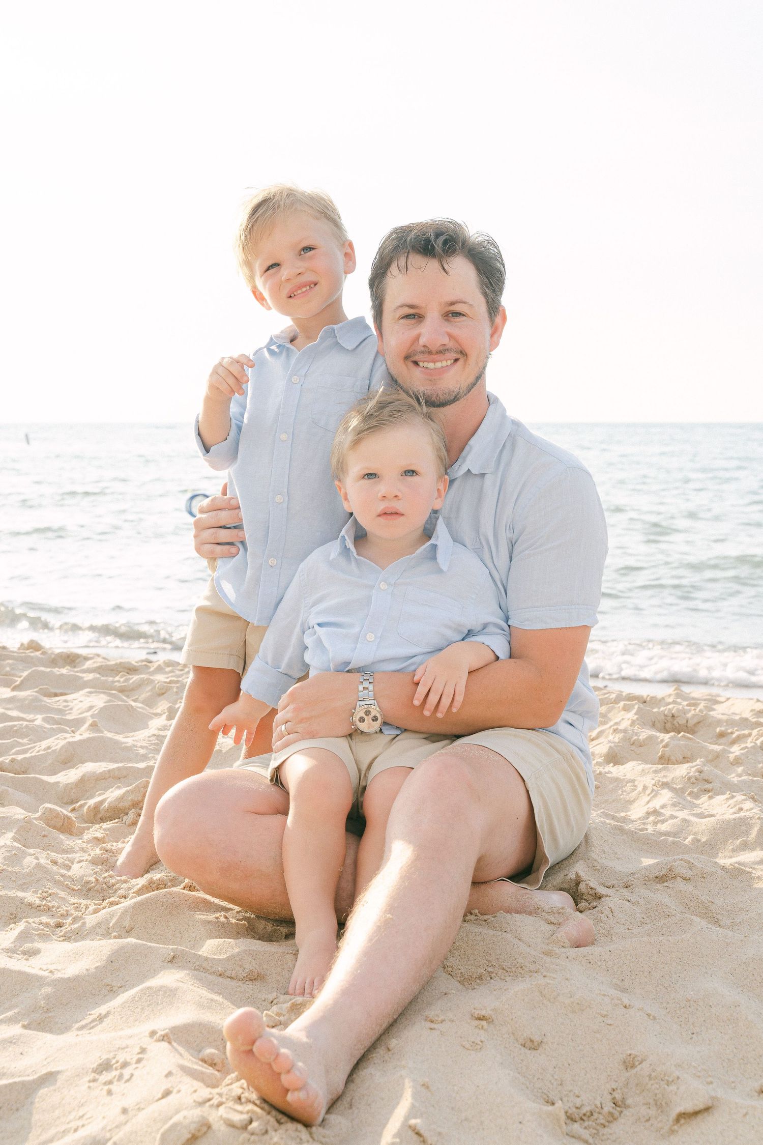 A family sits together on a sunny beach with ocean waves in the background.