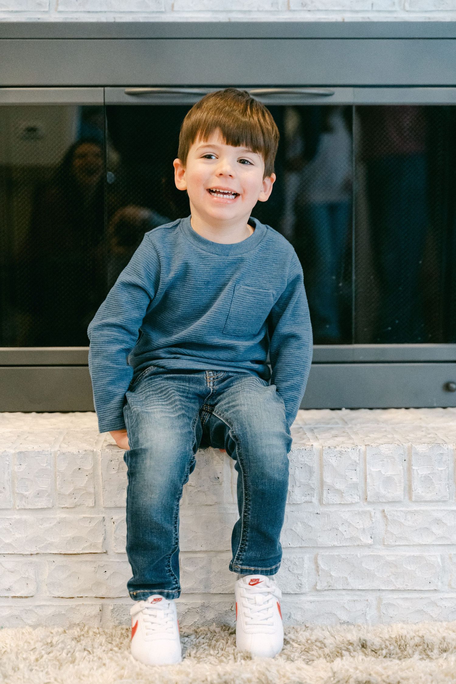 A young child in blue sweater and jeans sits casually on a brick ledge.