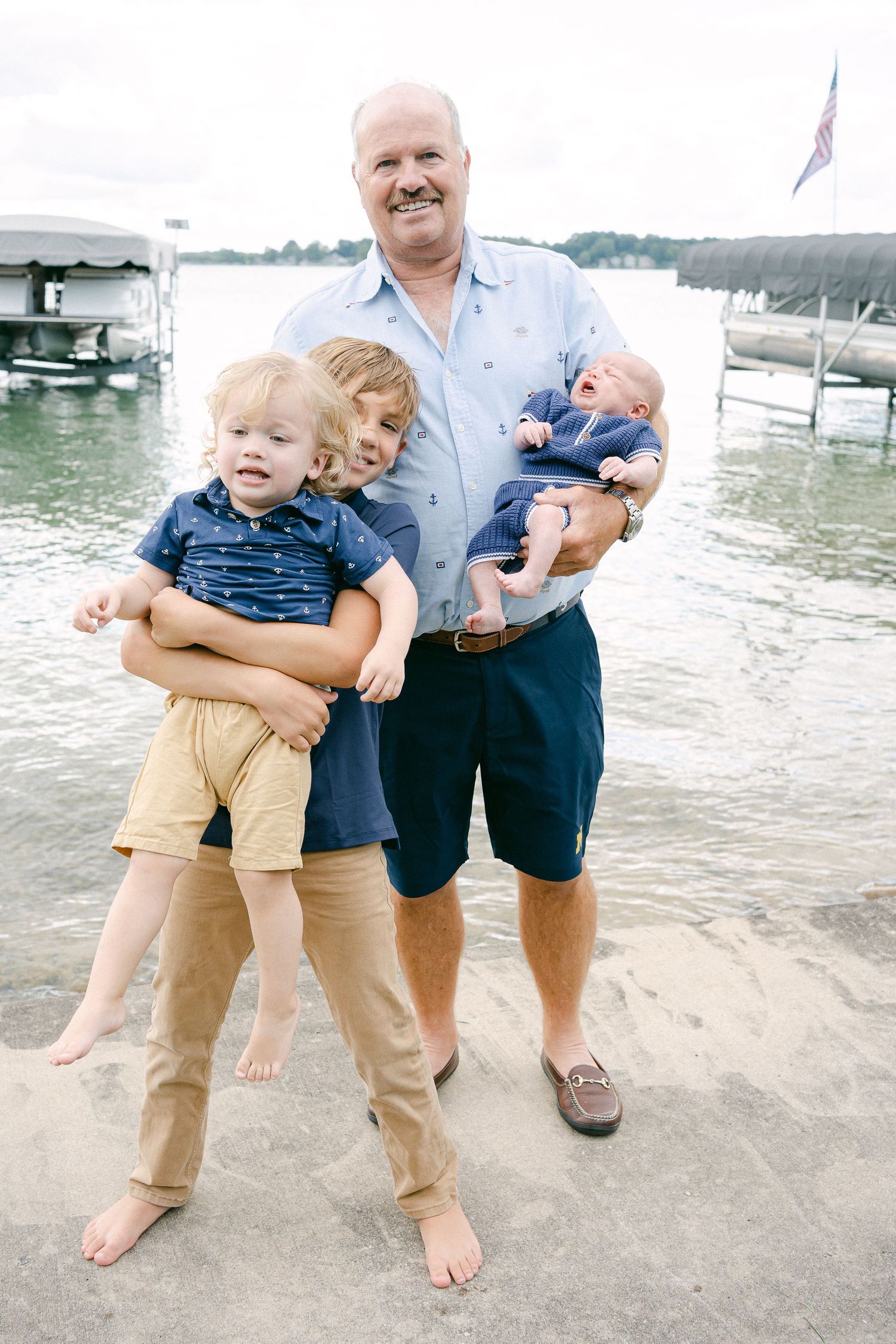 A waterfront family portrait with a marina and boats visible in the background on a sunny day.