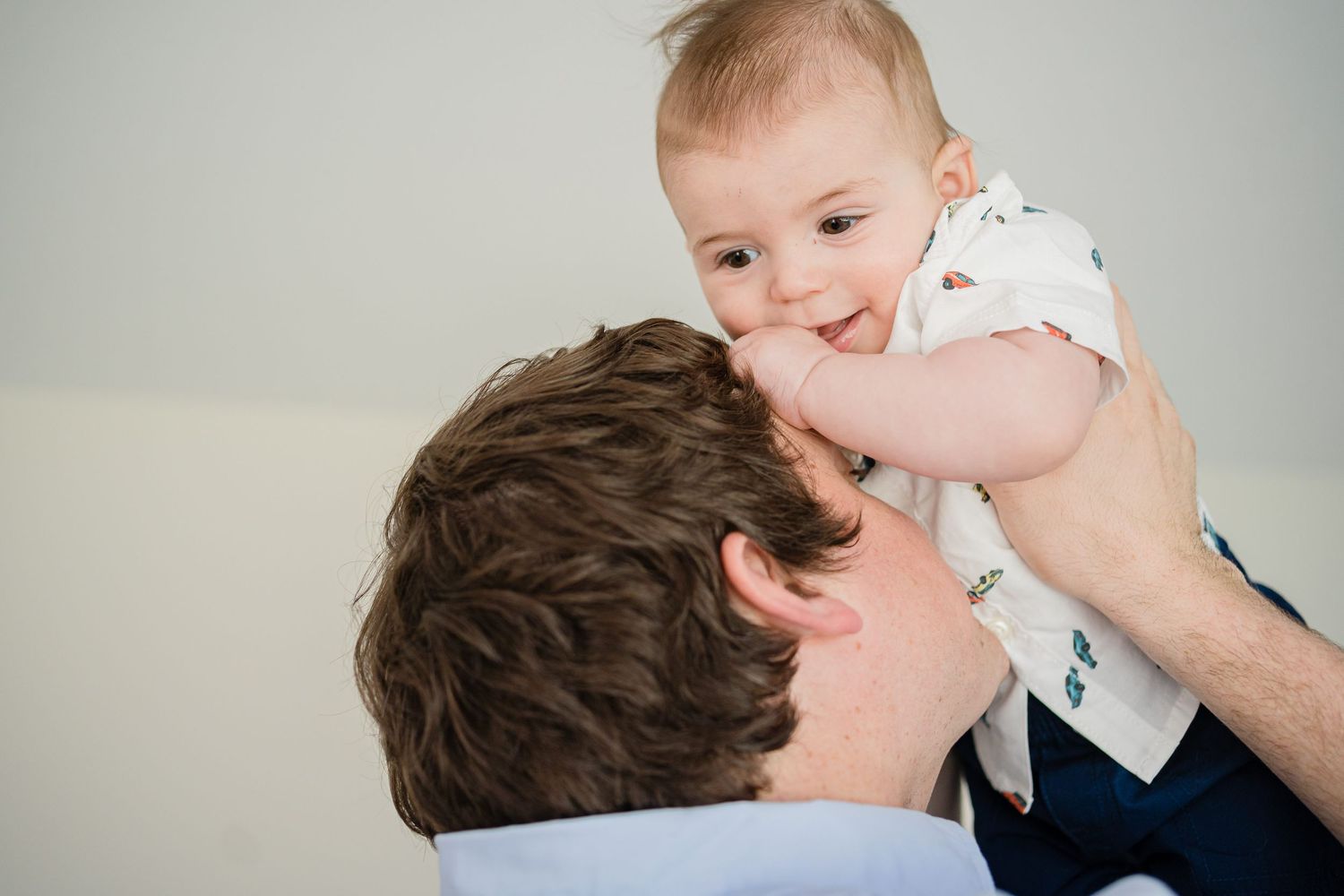 A tender moment between parent and baby as they share a playful interaction against a light background.