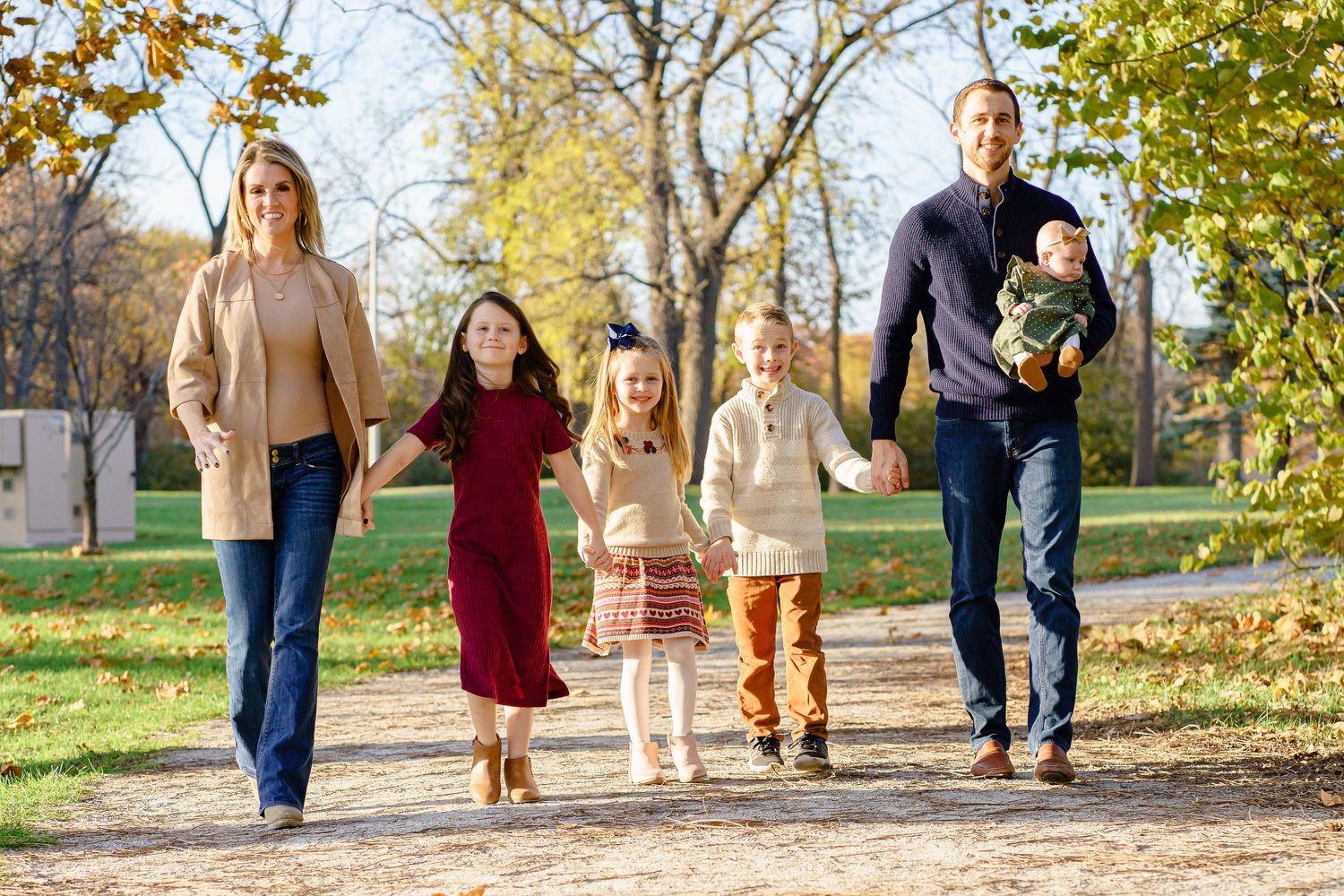 A family walking together on a tree-lined autumn path with fallen leaves and golden foliage.