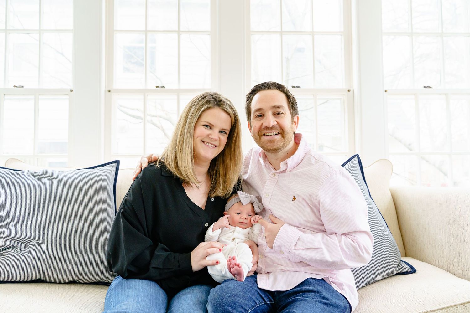 Happy family sitting together on white couch in bright sunlit living room.