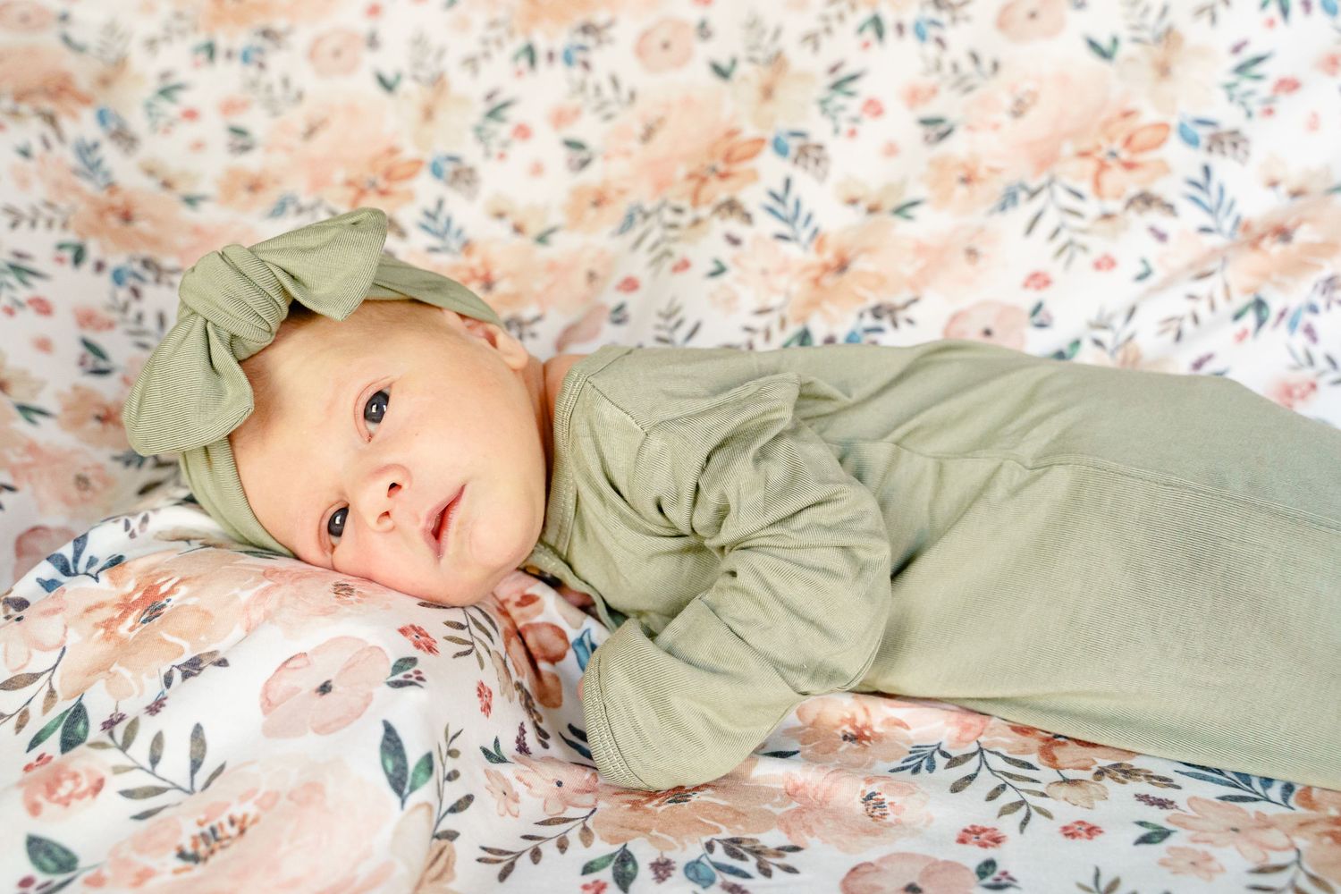 Baby lying on floral bedding wearing sage green outfit.