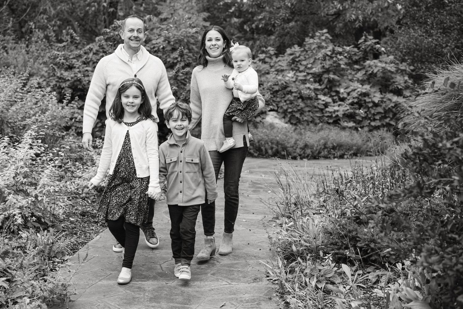 A candid family photo session in a lush garden setting with natural greenery and walking paths.
