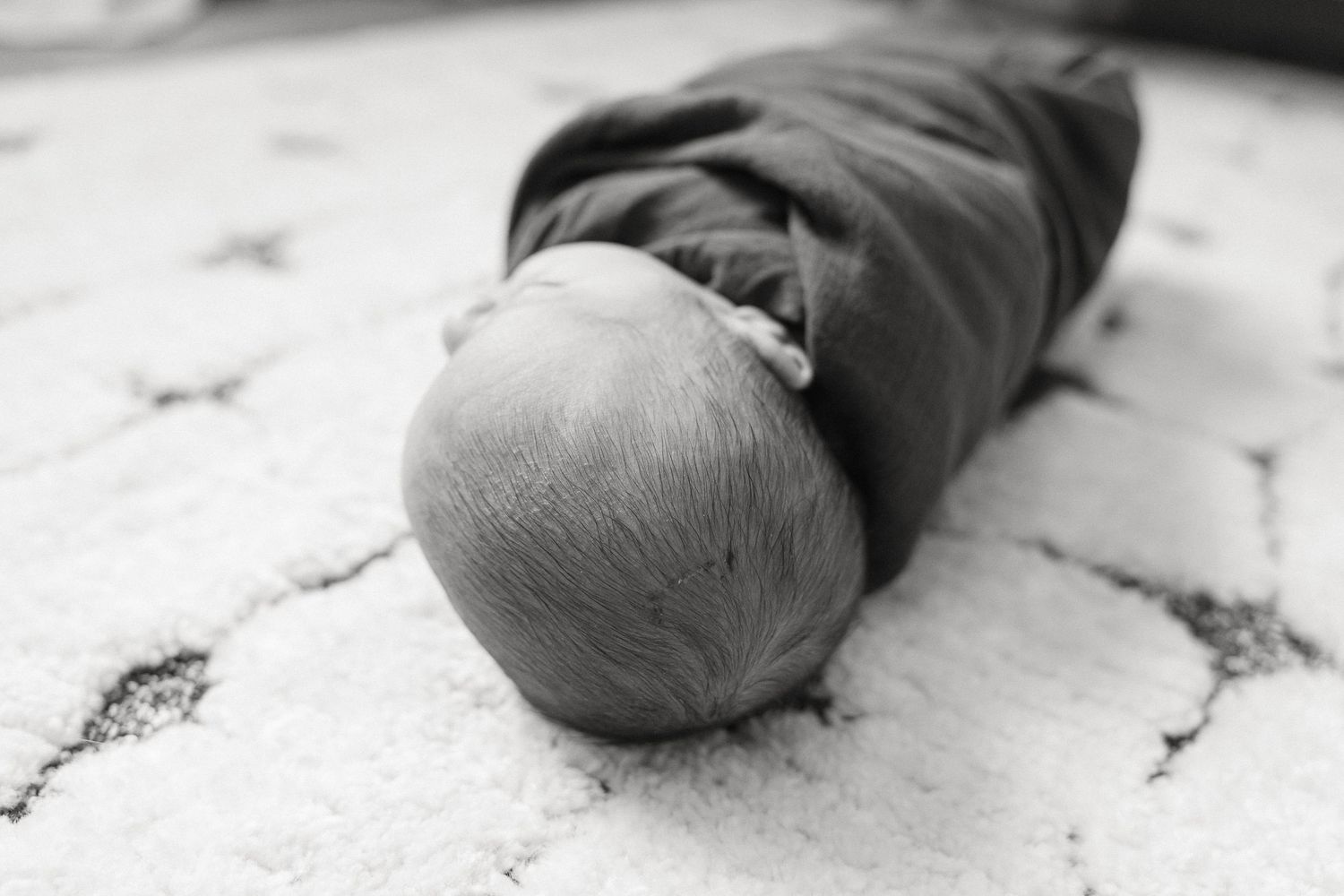 Black and white close-up of a swaddled newborn baby sleeping on patterned fabric.