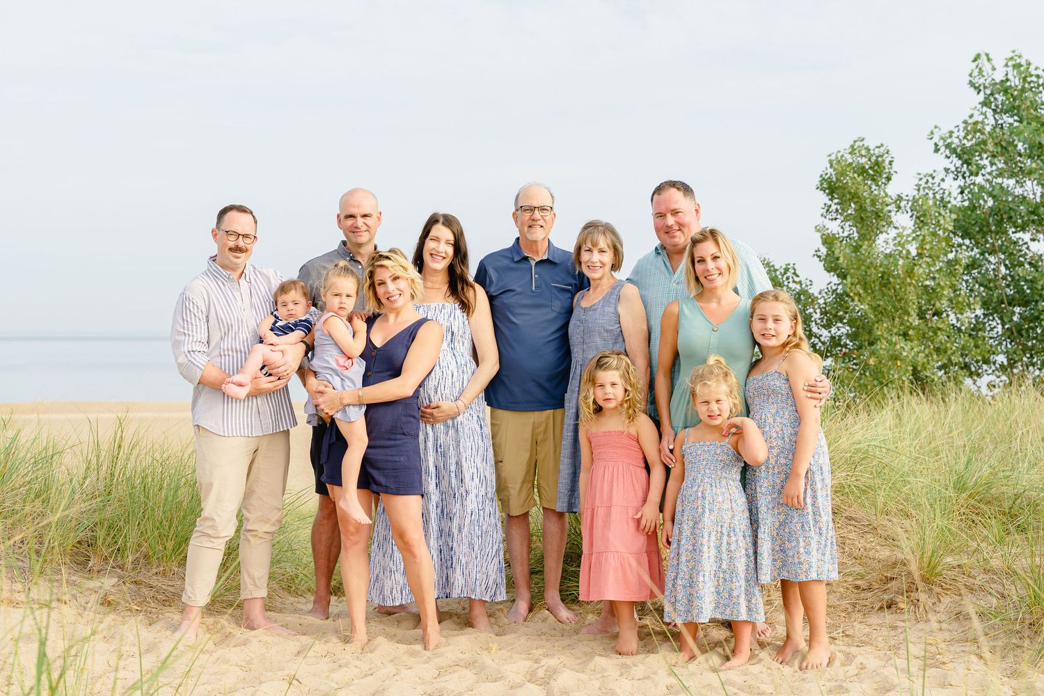 A group poses together on a sandy beach path wearing coordinated casual summer outfits in soft pastel colors.