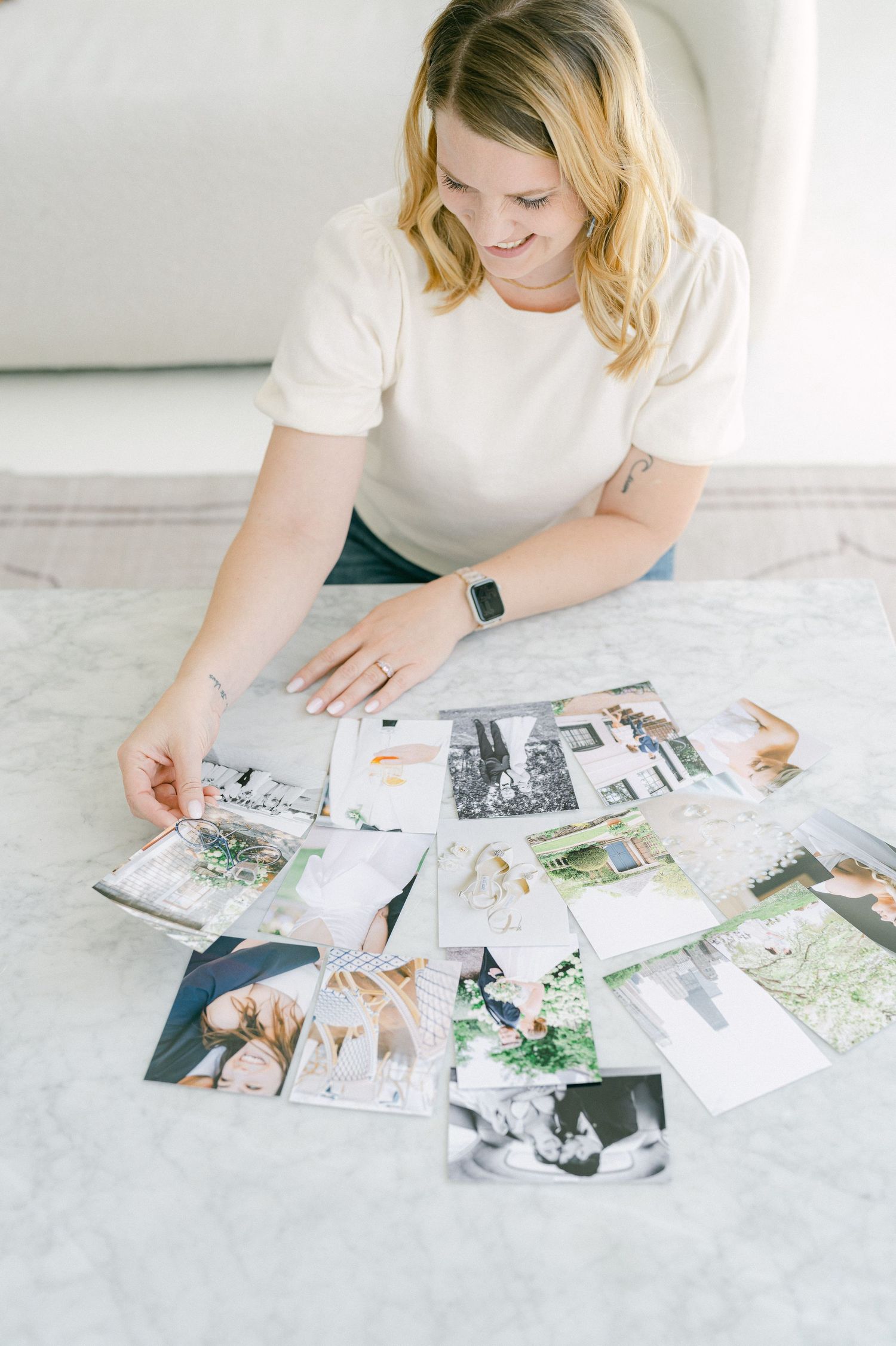 Someone in a white t-shirt looks through a collection of printed photographs spread out on a marble surface.
