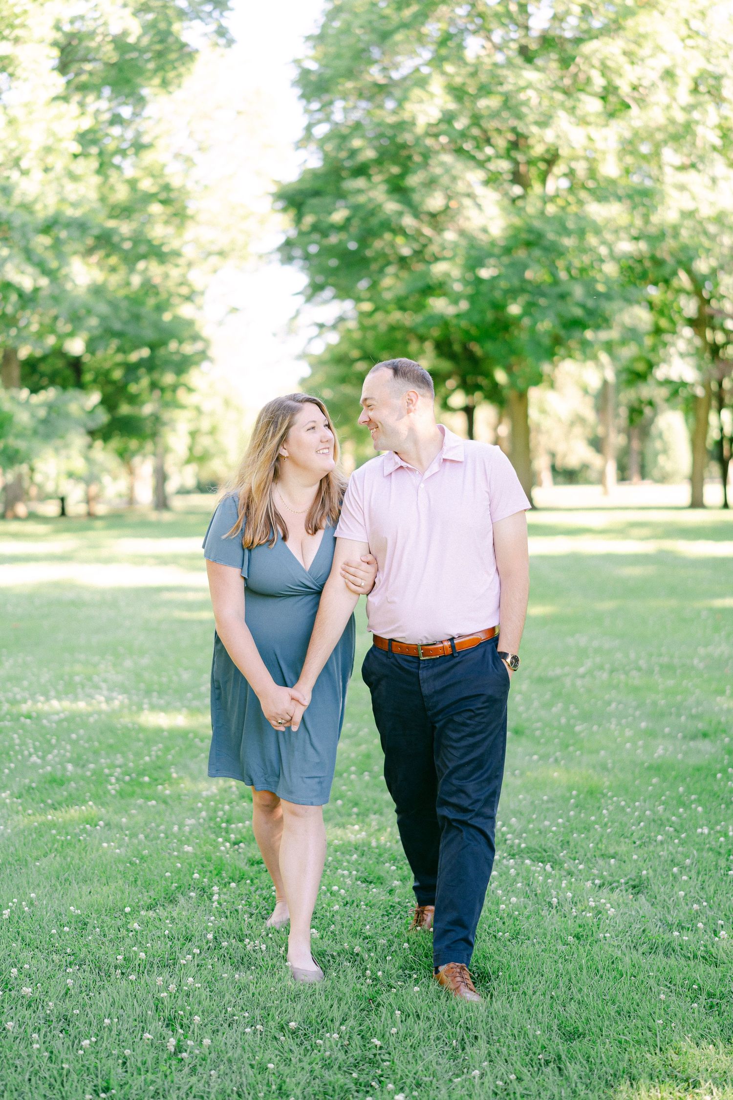 A couple walks hand in hand through a sunlit park on a summer afternoon.