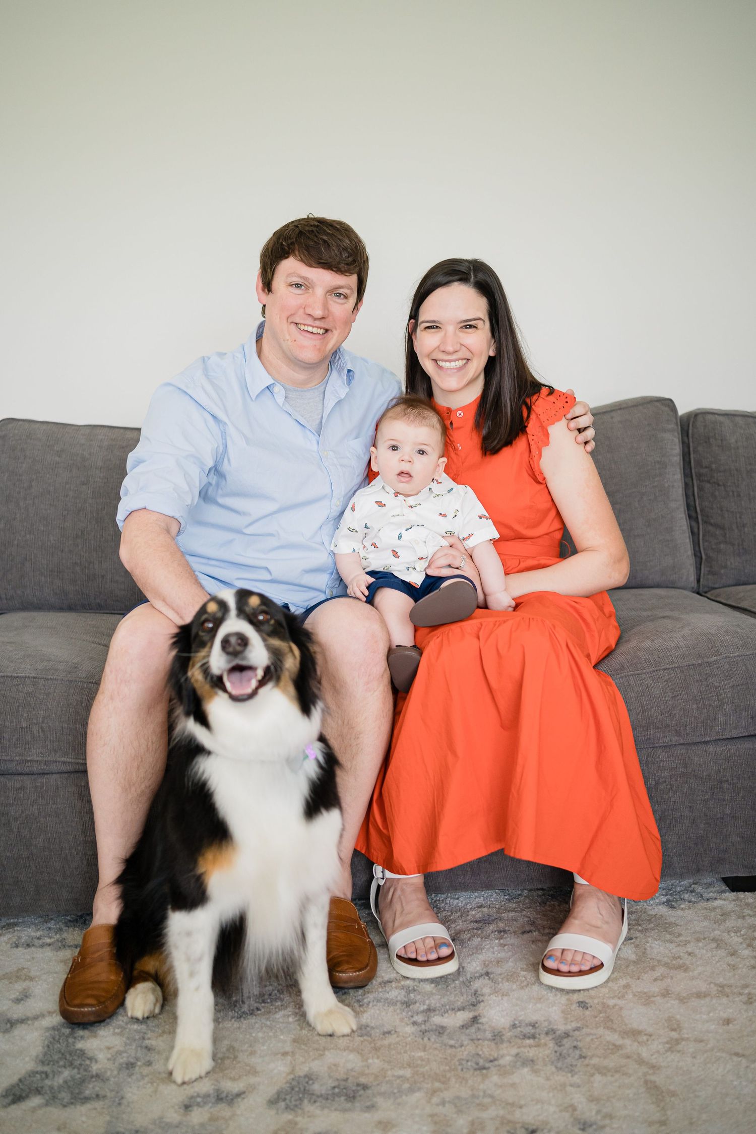 A family and their Australian Shepherd dog pose together on a gray couch in a series of casual indoor portraits.