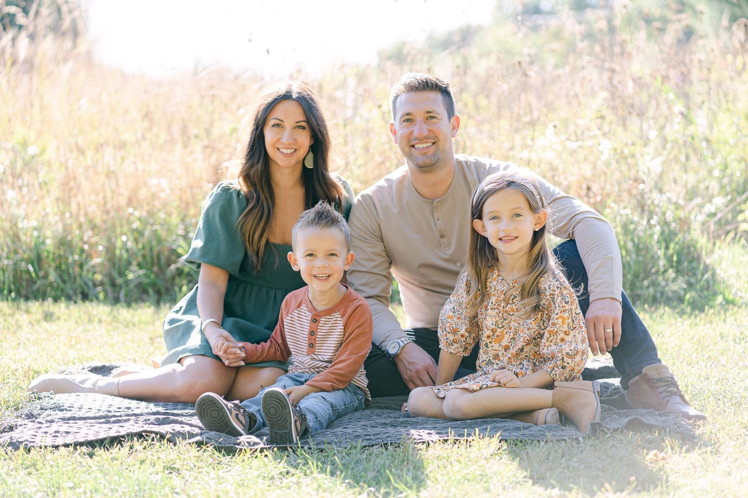 A family lying together on grass in golden sunlight during an outdoor photo session.