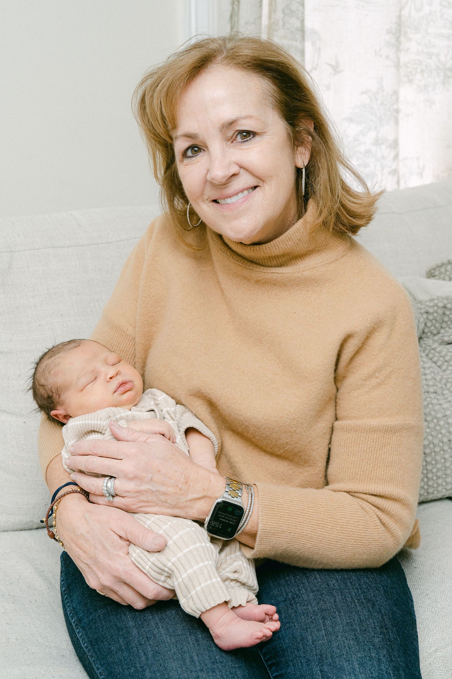 A person in a tan sweater cradles and bonds with their sleeping newborn baby in a cozy home environment.