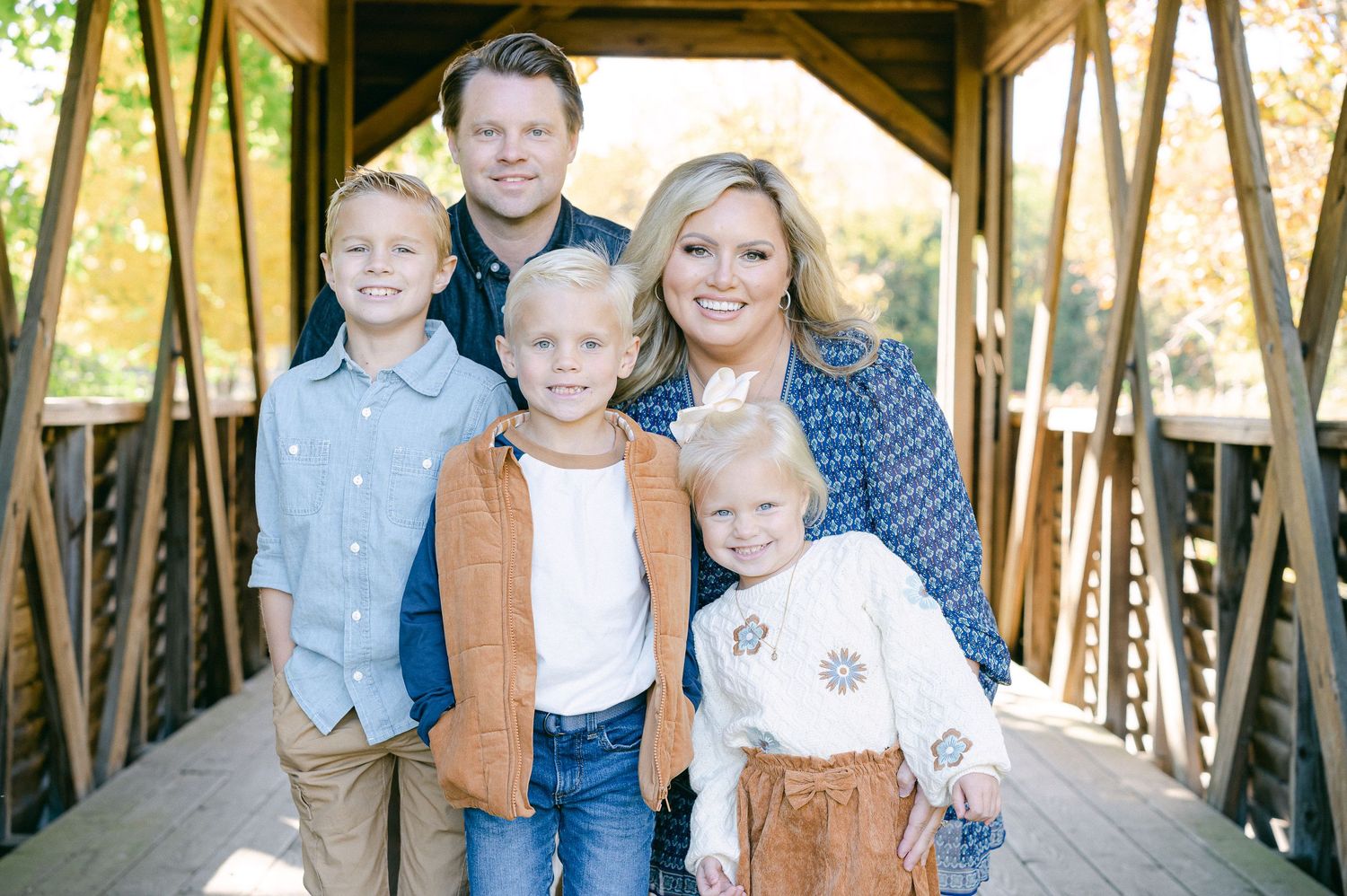 Family poses together for a portrait session under a rustic wooden covered bridge in autumn.