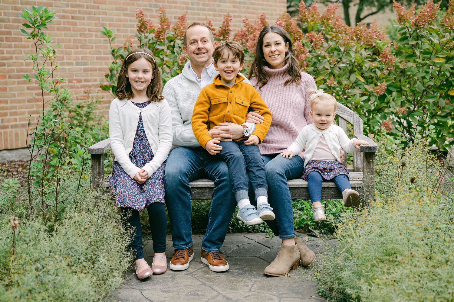 A group sits together on a brick wall surrounded by lush greenery and autumn foliage.