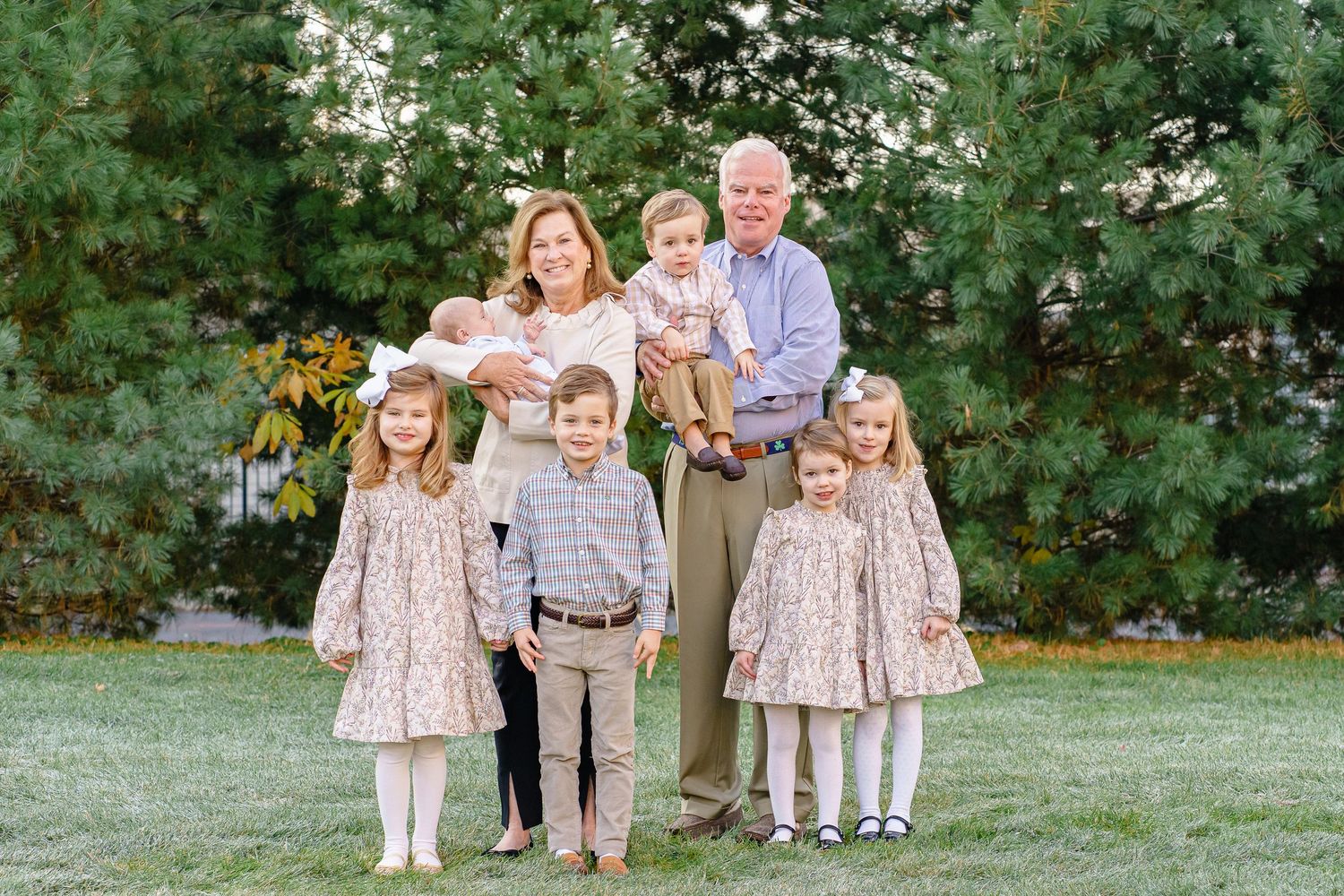 Family group poses together outdoors in coordinated outfits against lush green foliage background.