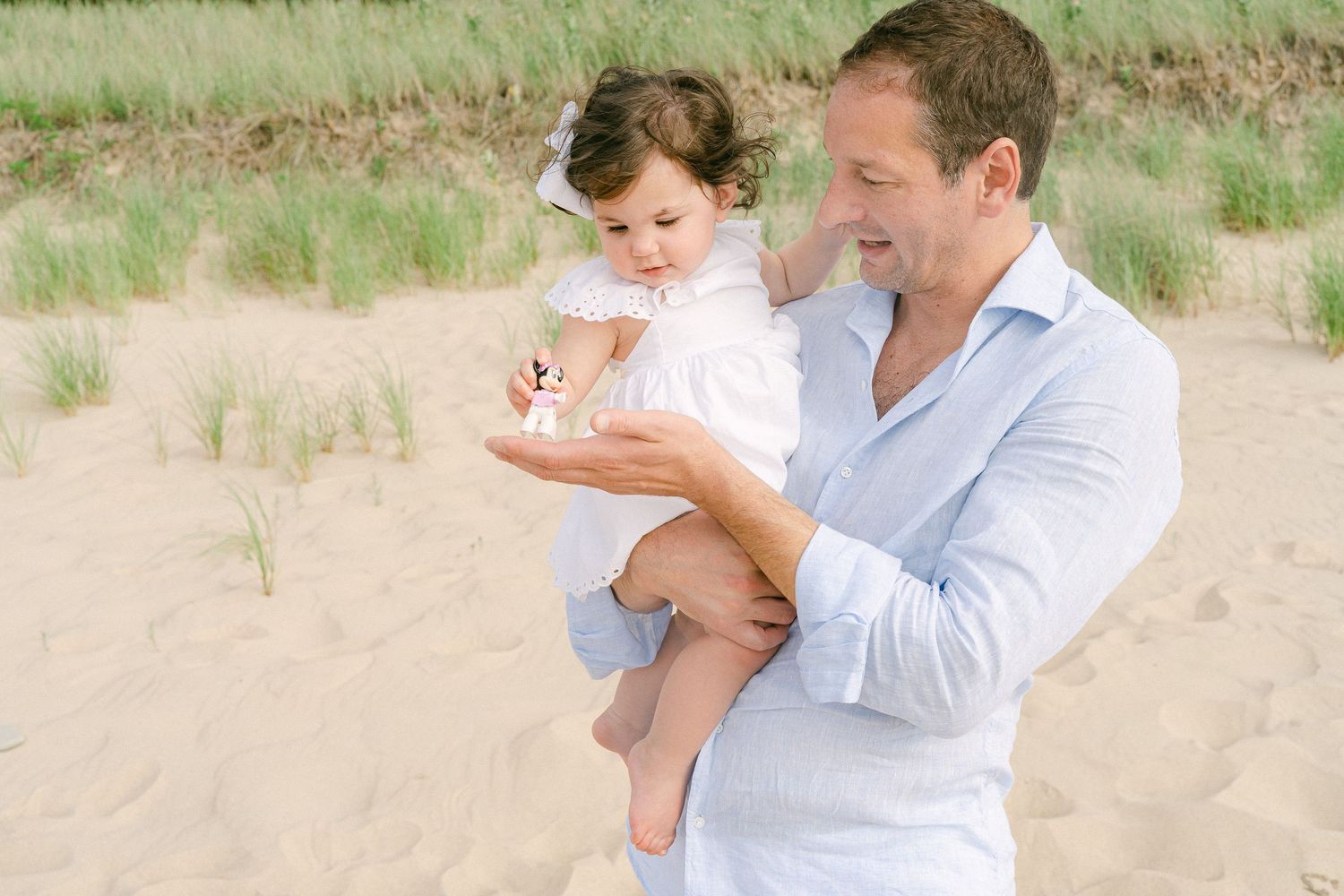 A family shares tender moments together on a sandy beach wearing light blue and white clothing.