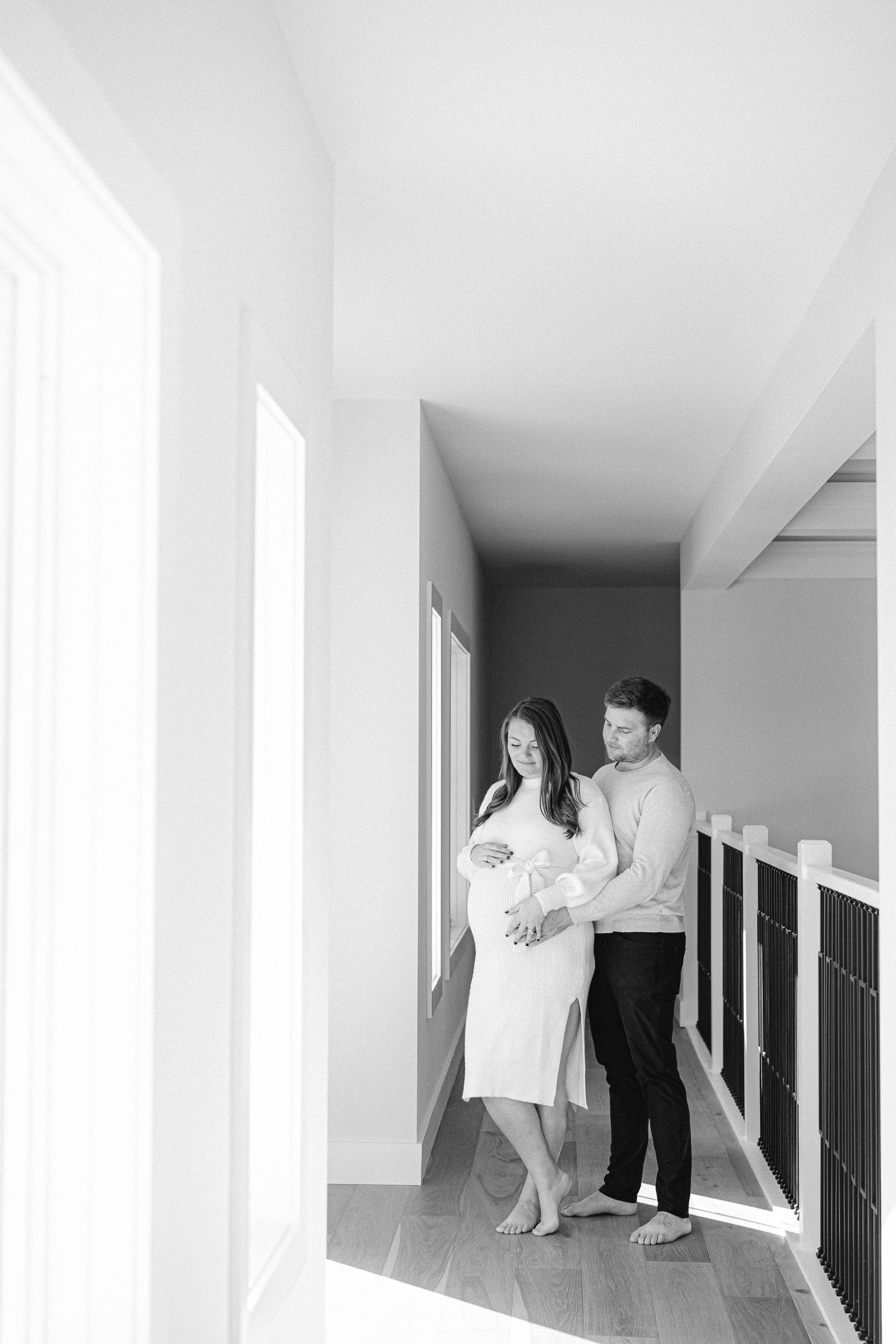 Couple stands in bright hallway during intimate maternity photoshoot.