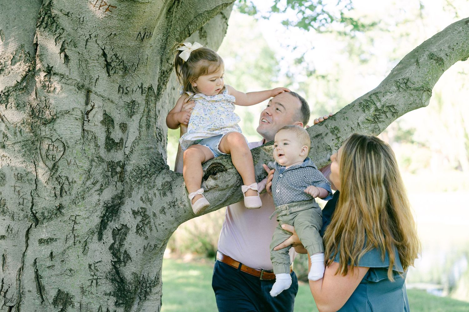 A tender family moment captured outdoors against a large tree trunk in natural lighting.