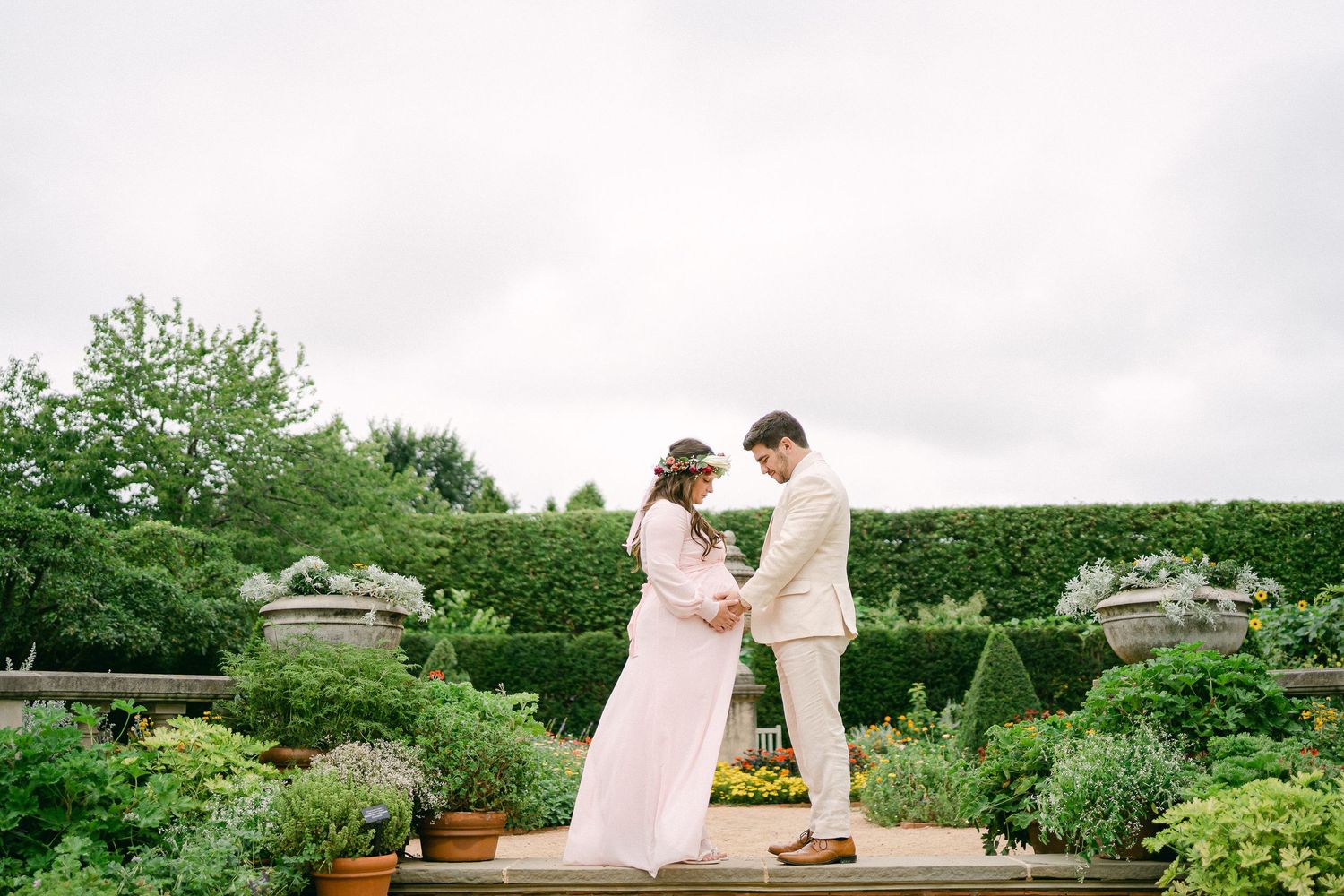 A couple shares a romantic moment in a lush garden setting with manicured hedges and blooming flowers.